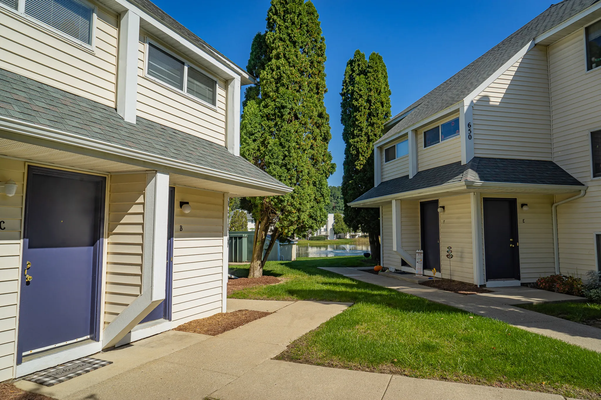 Charming townhouse community with well-maintained landscaping, inviting front entrances, and scenic views of lush greenery and water feature.