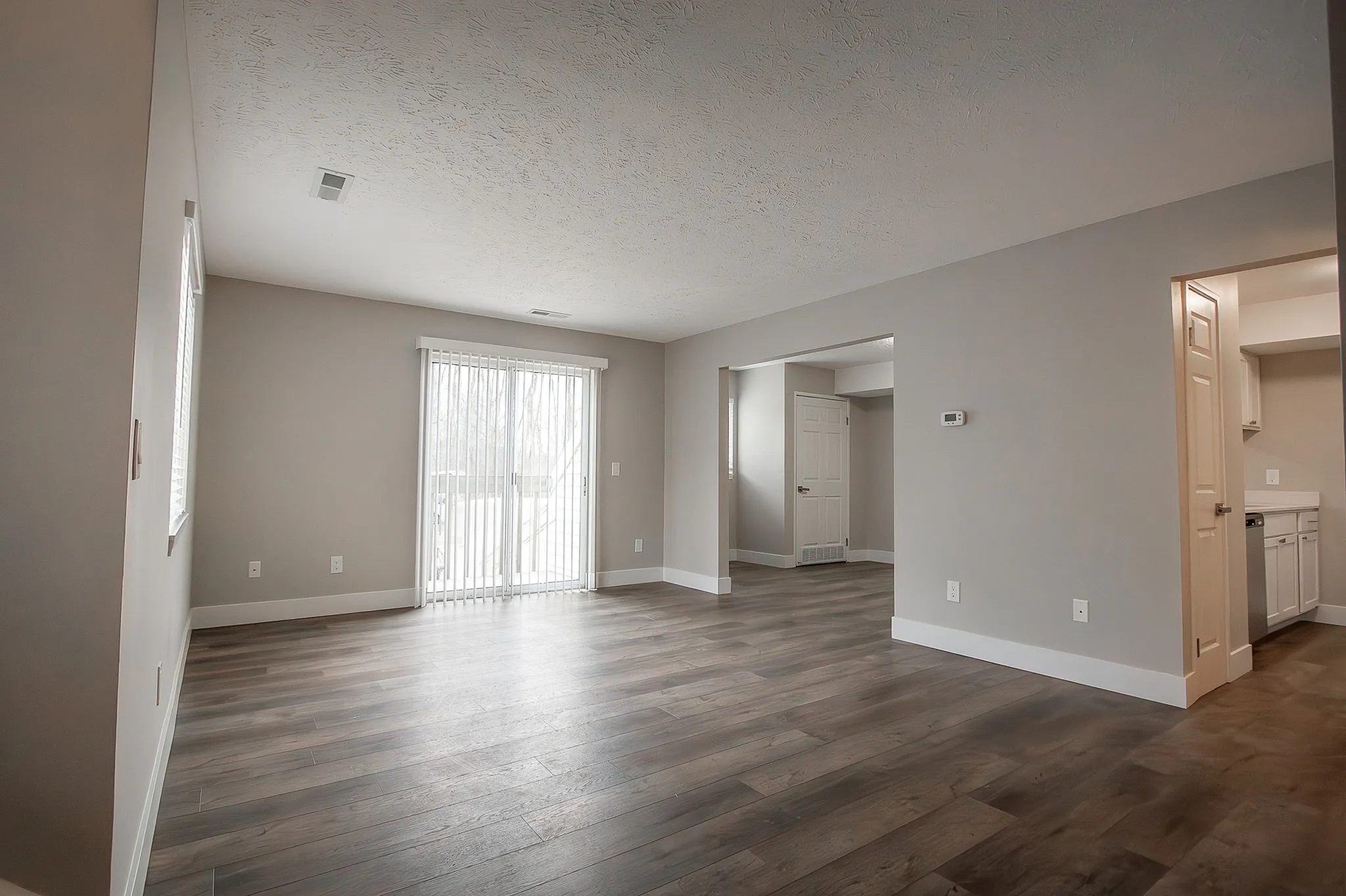 Modern open-concept living area in an apartment with sleek wood flooring and natural light from large patio doors.