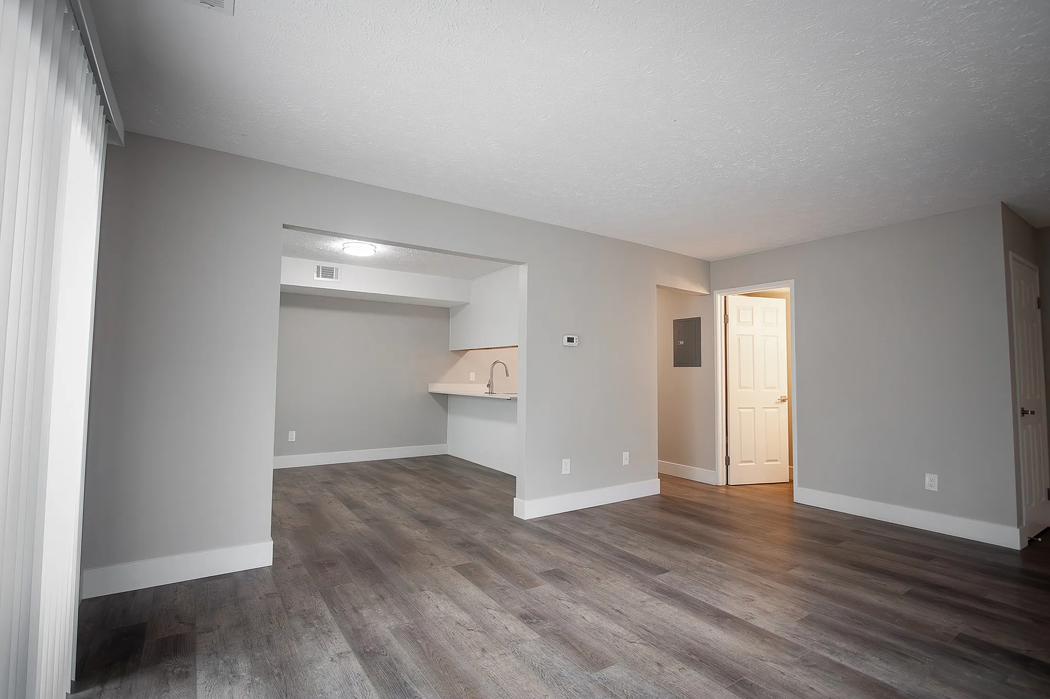 Elegant open-plan living area with sleek dark wood flooring, modern kitchen alcove, and bright walls, offering ample space and style.