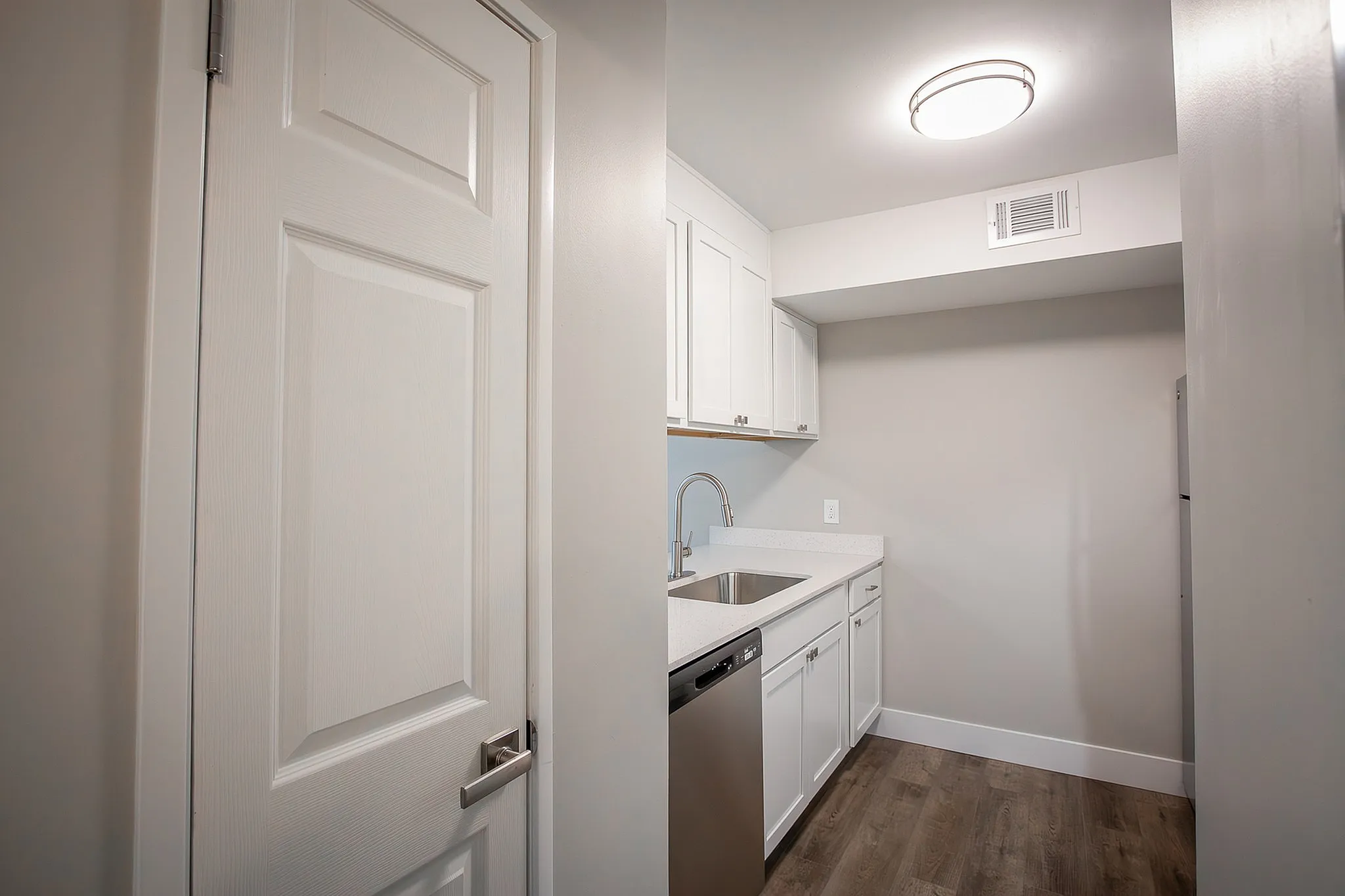Modern kitchen with sleek white cabinetry, stainless steel appliances, and elegant wood flooring, illuminated by a stylish ceiling light.