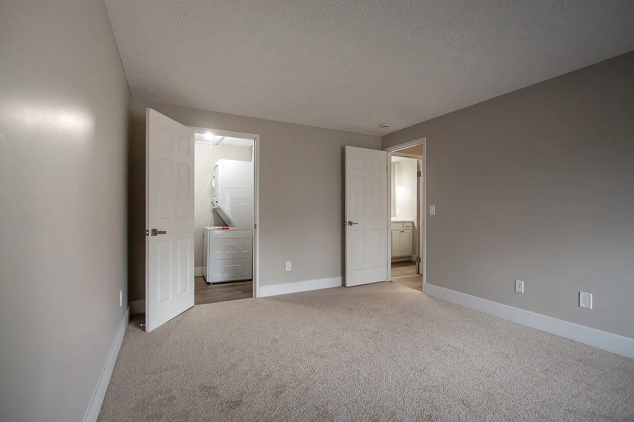 Bright and spacious bedroom with plush carpeting, featuring doors leading to a modern laundry area and elegant bathroom.