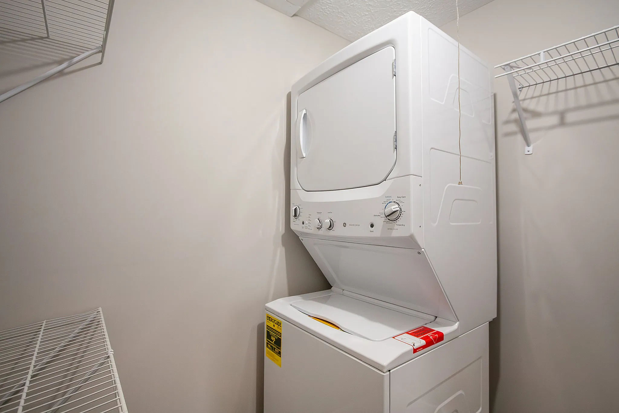 Modern laundry room featuring a sleek stacked washer and dryer unit with ample shelving for storage.