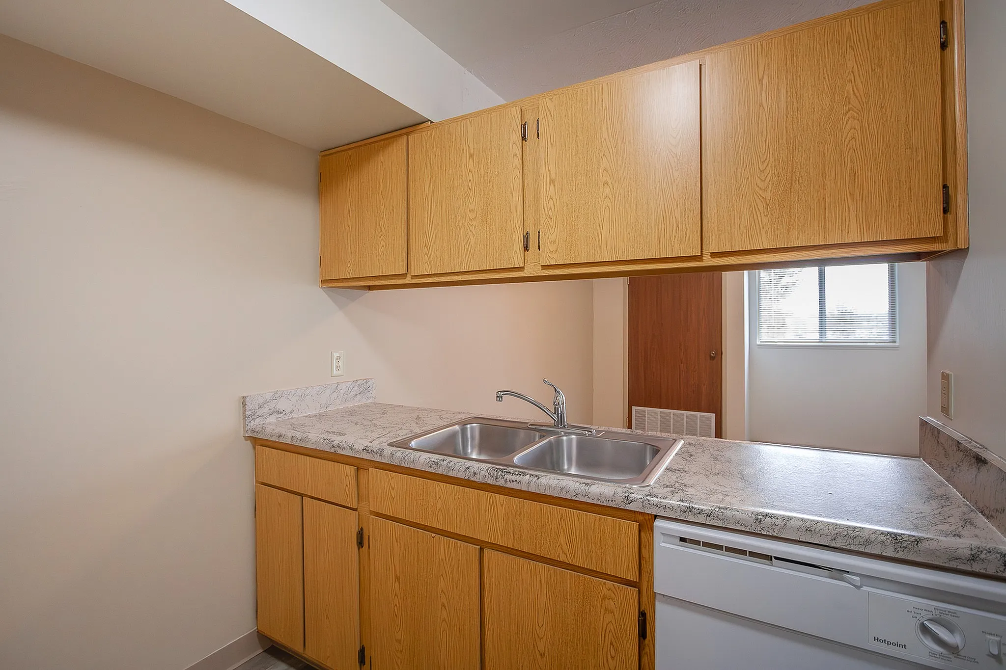 Bright and functional kitchen with sleek countertops, ample wooden cabinetry, and a double sink, ideal for home cooking.