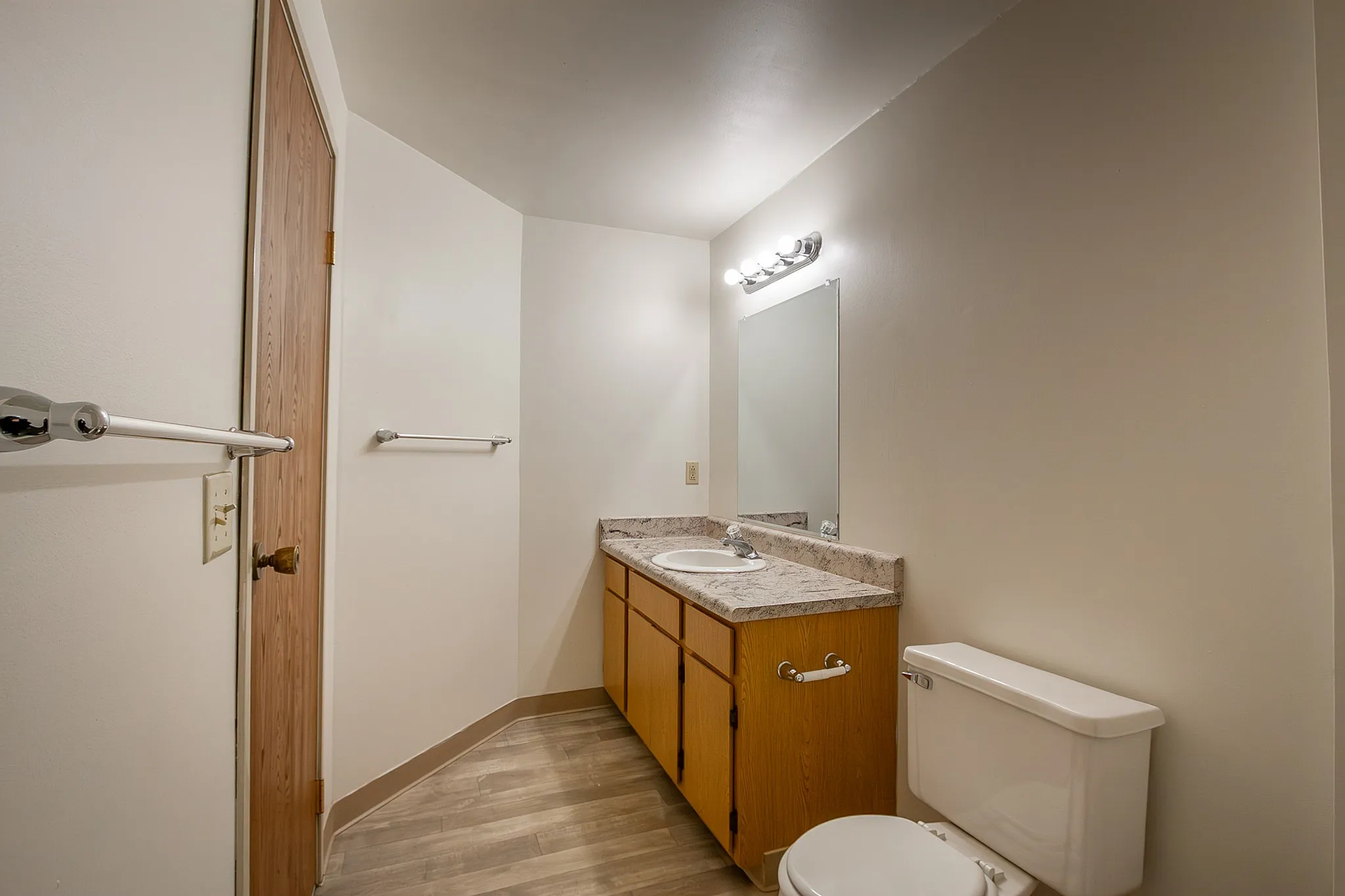 Bright and modern bathroom featuring sleek countertops, warm wood cabinetry, and a large mirror, perfect for a stylish living space.