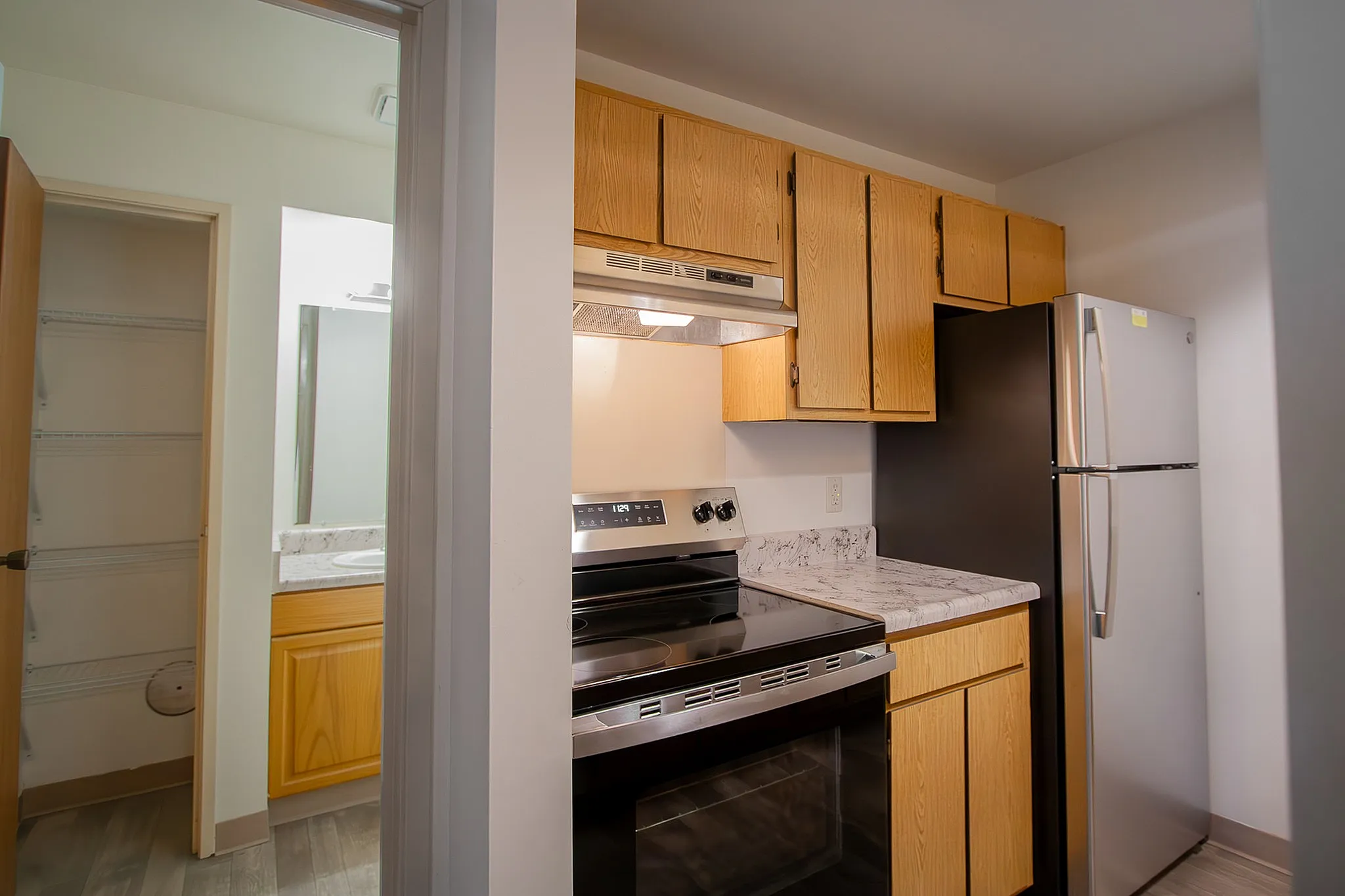 Modern kitchen space featuring sleek stainless steel appliances, elegant marble countertops, and warm wooden cabinets, adjoining a bright pantry and bathroom area.