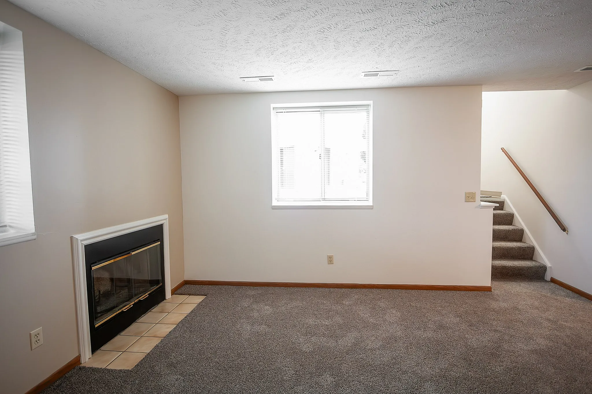 Inviting living room with plush carpet, cozy fireplace, and natural light from large windows, perfect for relaxation.