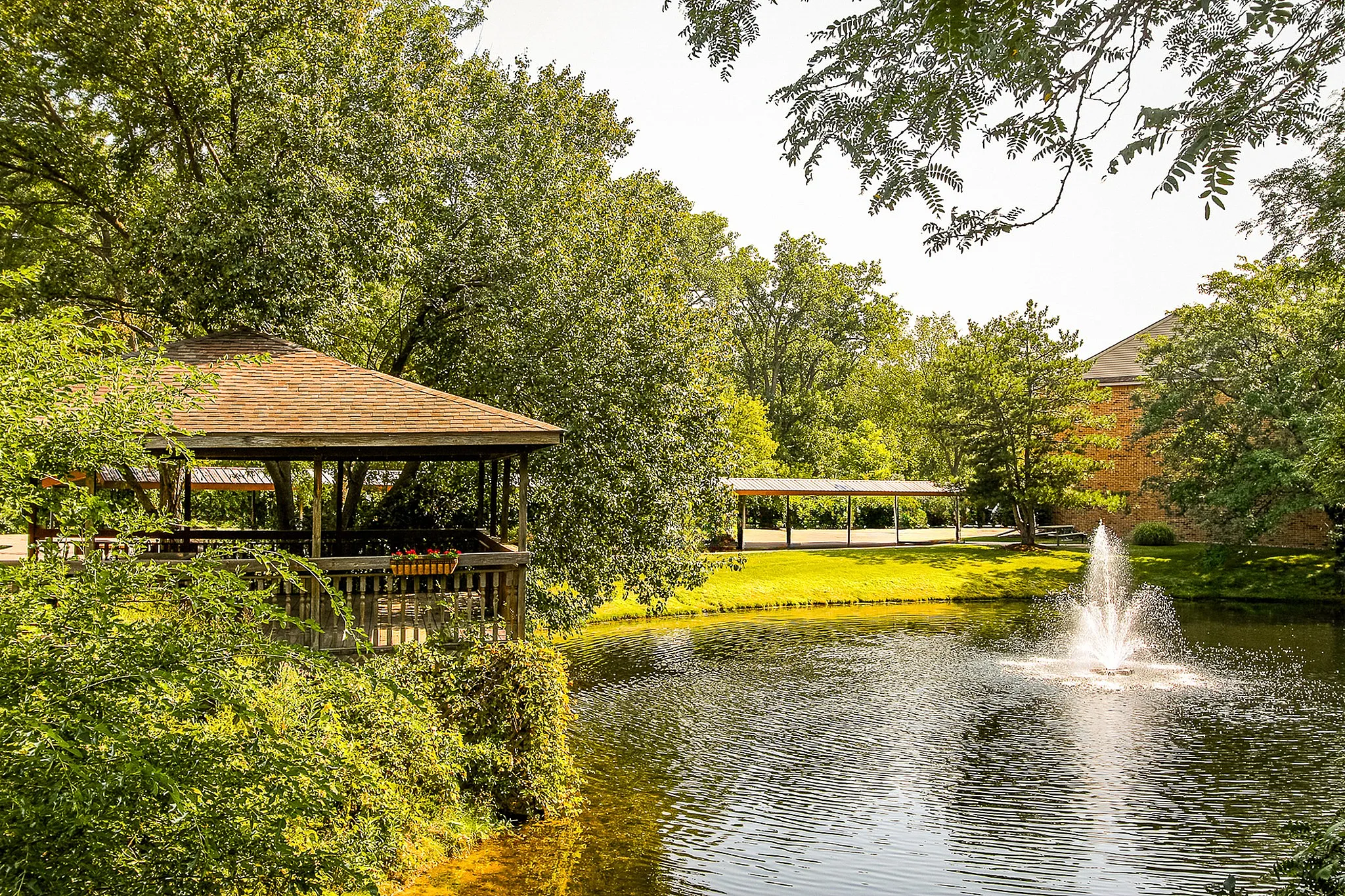 Serene pond view with a charming gazebo surrounded by lush greenery and a sparkling fountain, perfect for relaxation.