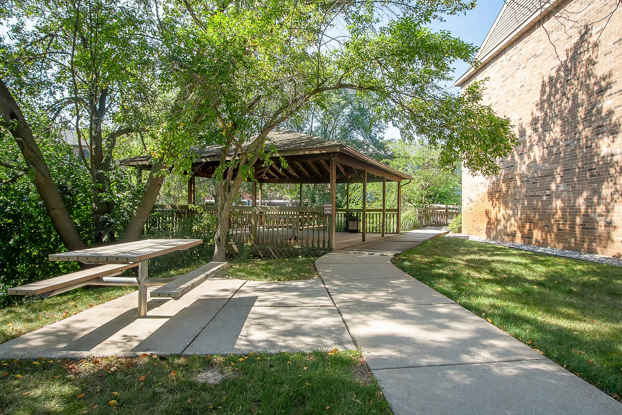 Charming outdoor area with a shady gazebo, surrounded by lush greenery and a convenient picnic table for relaxing.