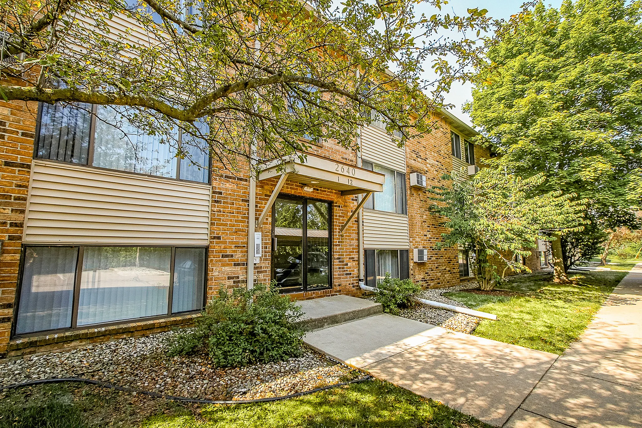 Charming brick apartment building with lush greenery, large windows, and inviting entrance.