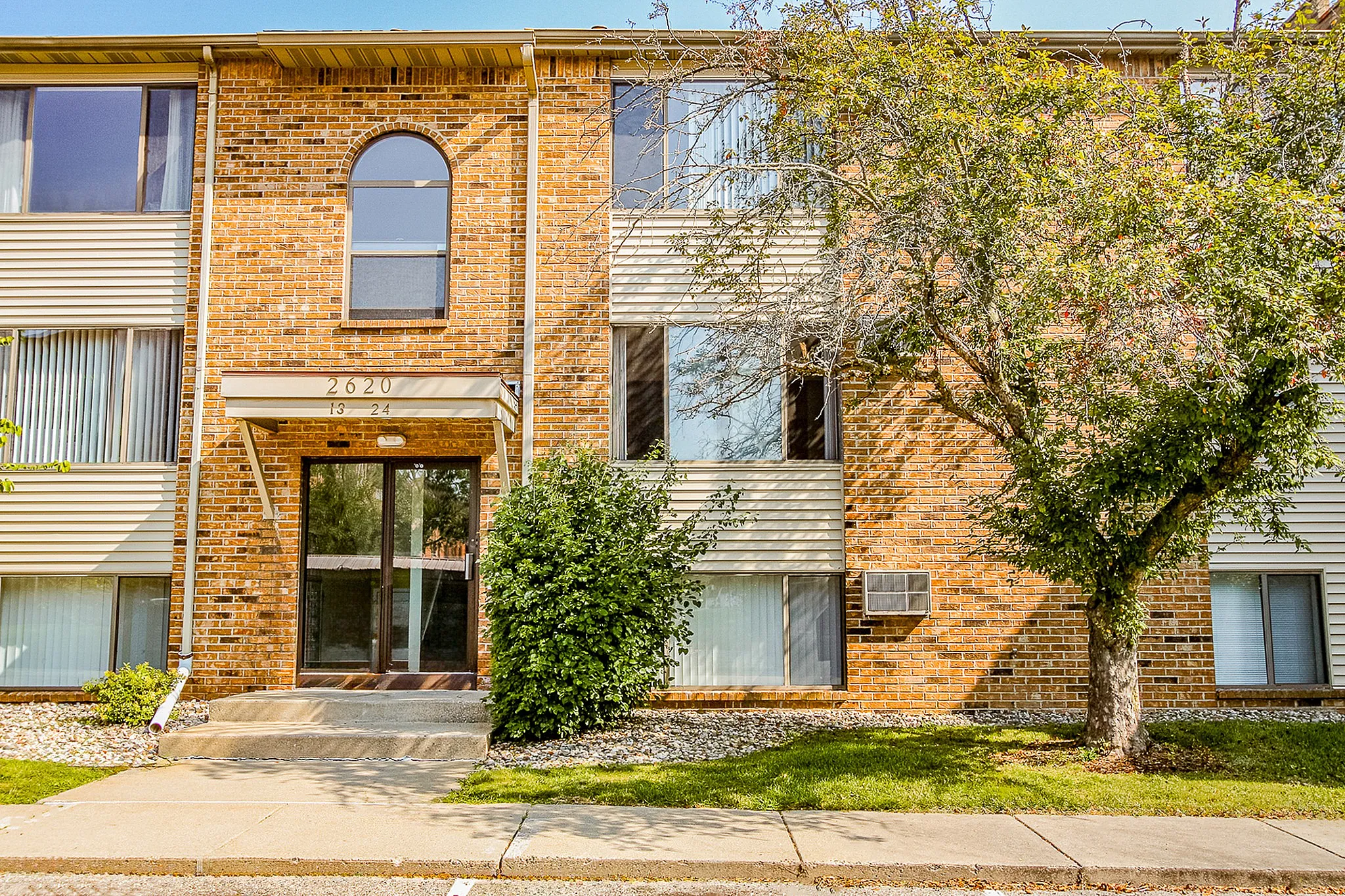 Charming brick apartment building with large windows, lush greenery, and inviting entrance.