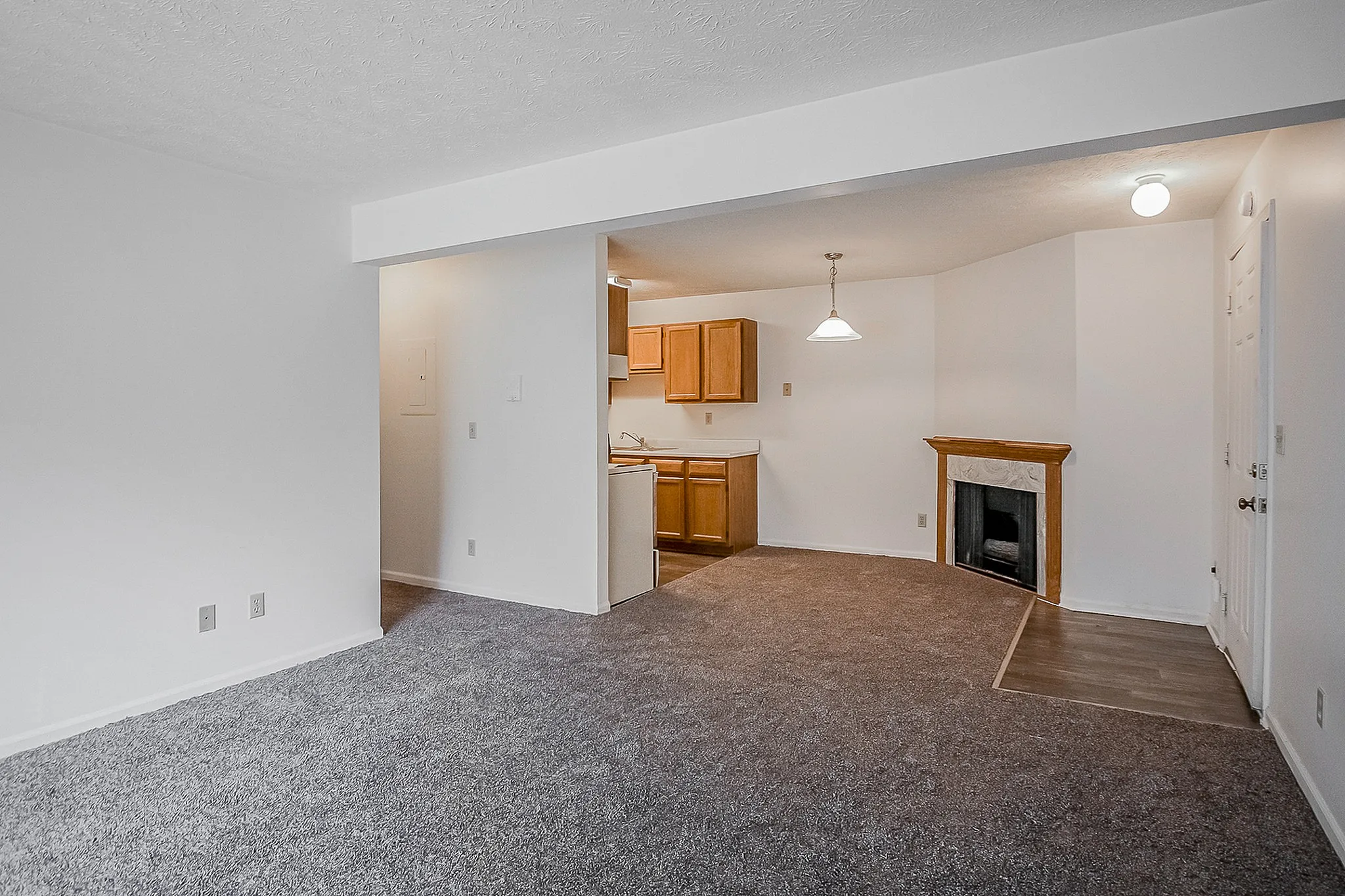 Inviting open-plan living room with plush carpeting, cozy fireplace, and a view into the modern kitchen with warm wooden cabinets.