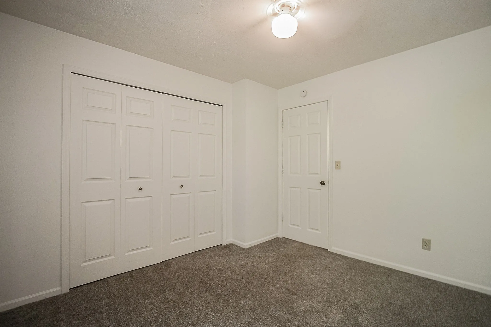 Bright, modern room featuring a spacious closet with double doors and fresh carpeting, ideal for a cozy bedroom.