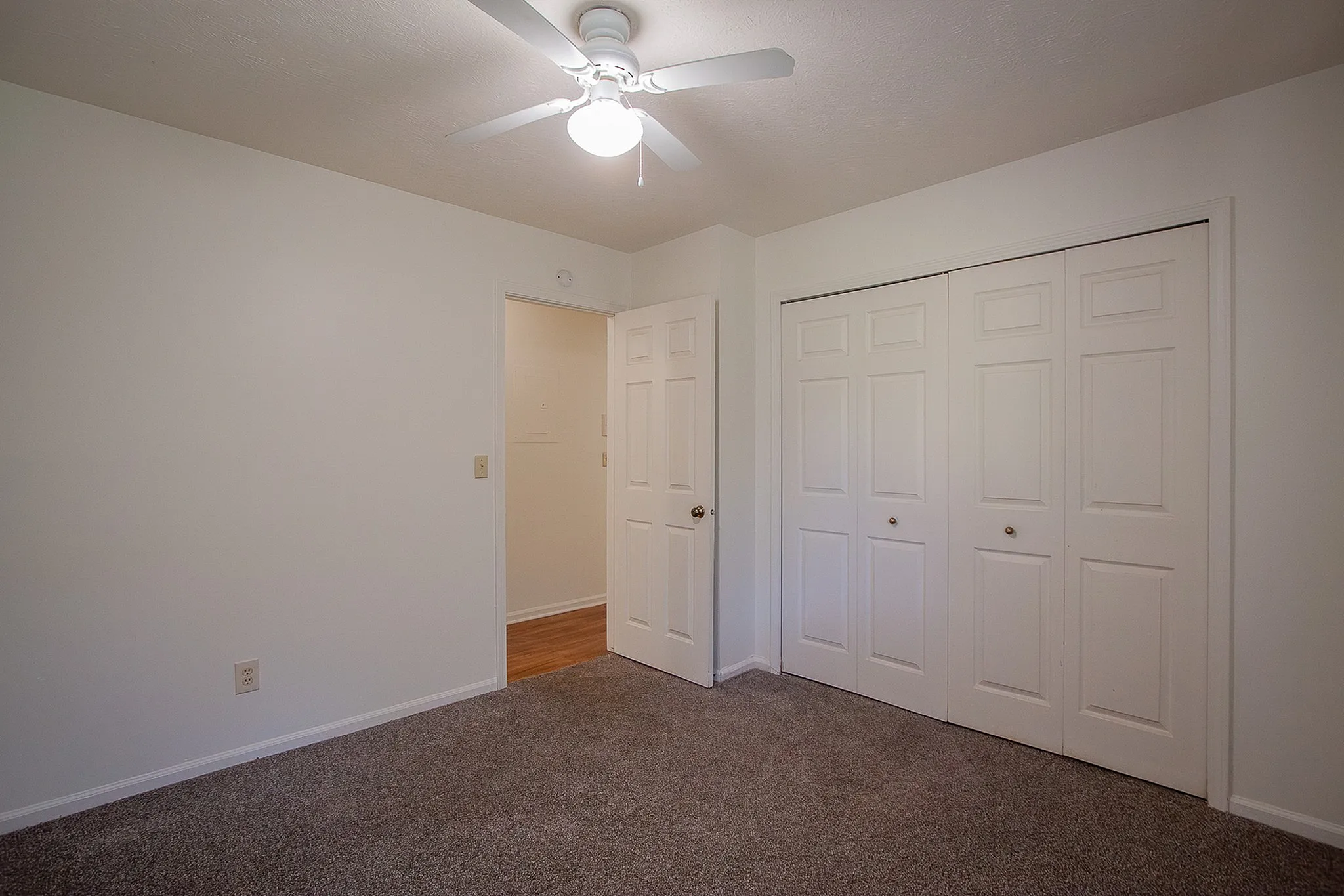 Inviting bedroom with plush carpet, ample closet space, and bright white walls, complemented by a modern ceiling fan for a cozy atmosphere.