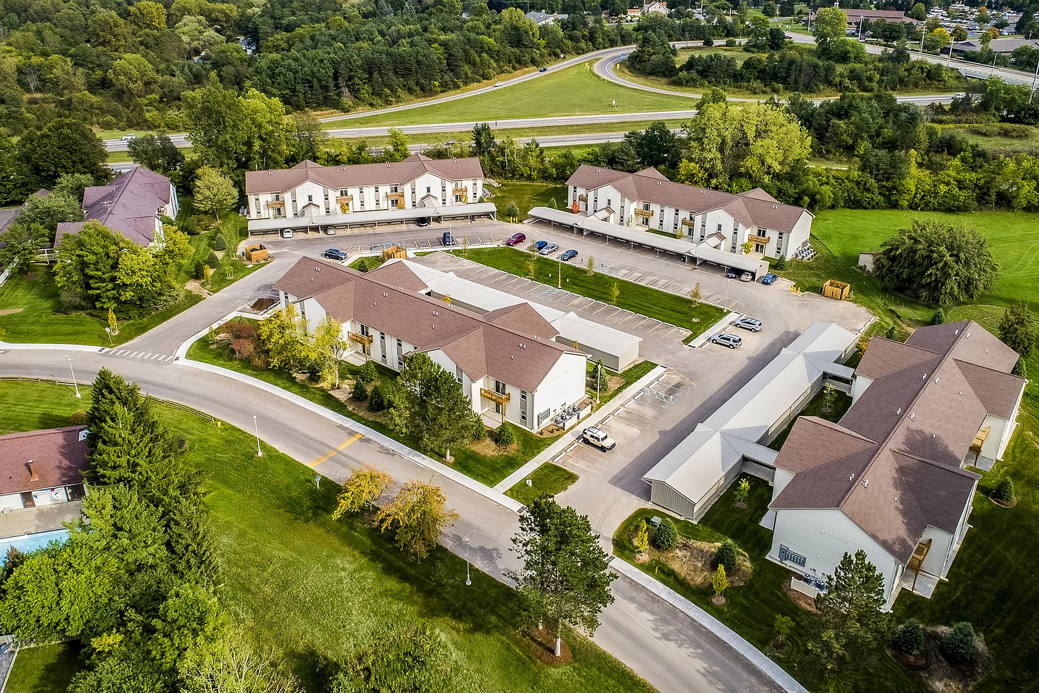 Charming aerial view of a serene apartment complex surrounded by lush greenery, featuring modern architecture and ample parking.