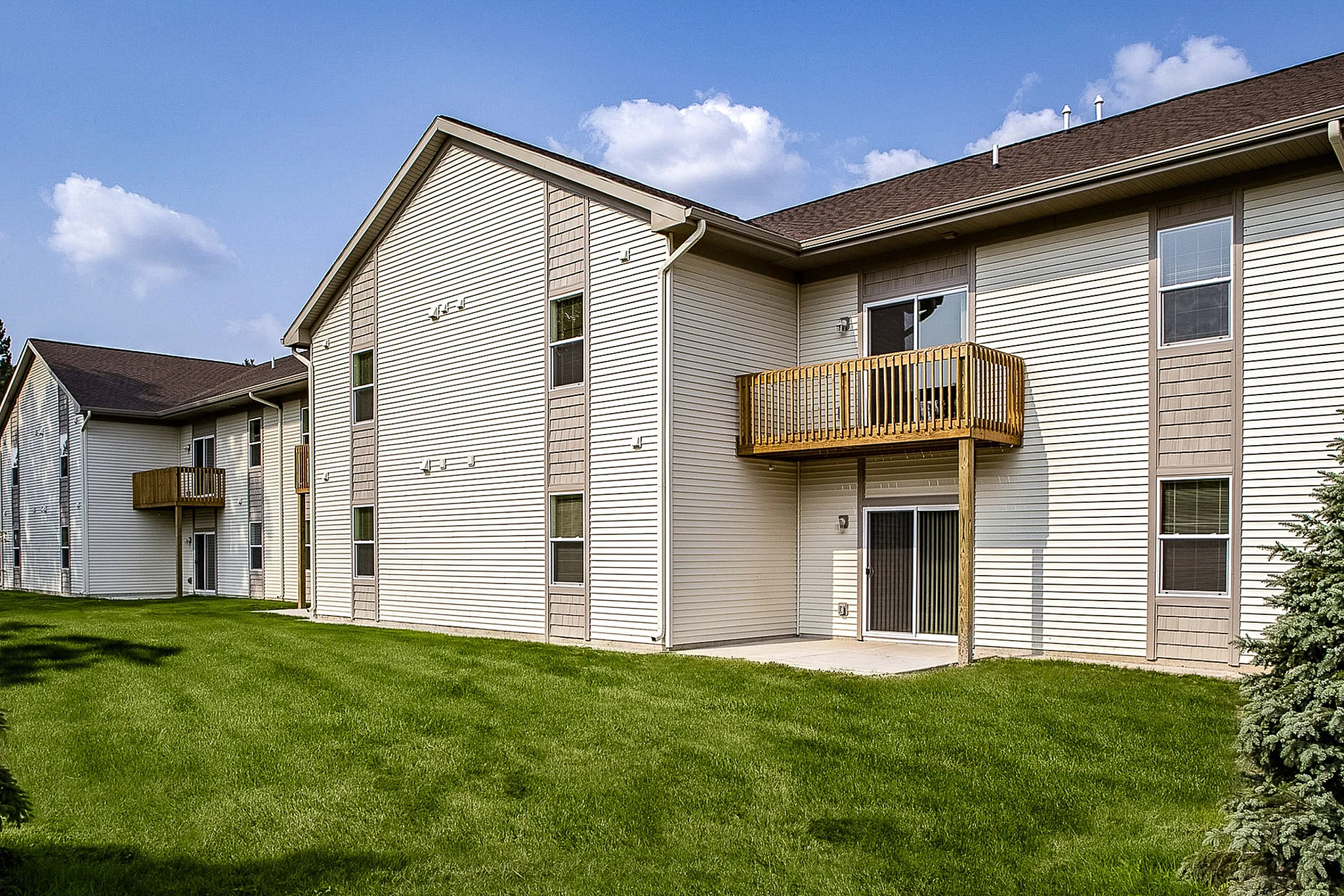 Charming apartment building with wooden balconies, surrounded by lush green grass and clear blue sky.