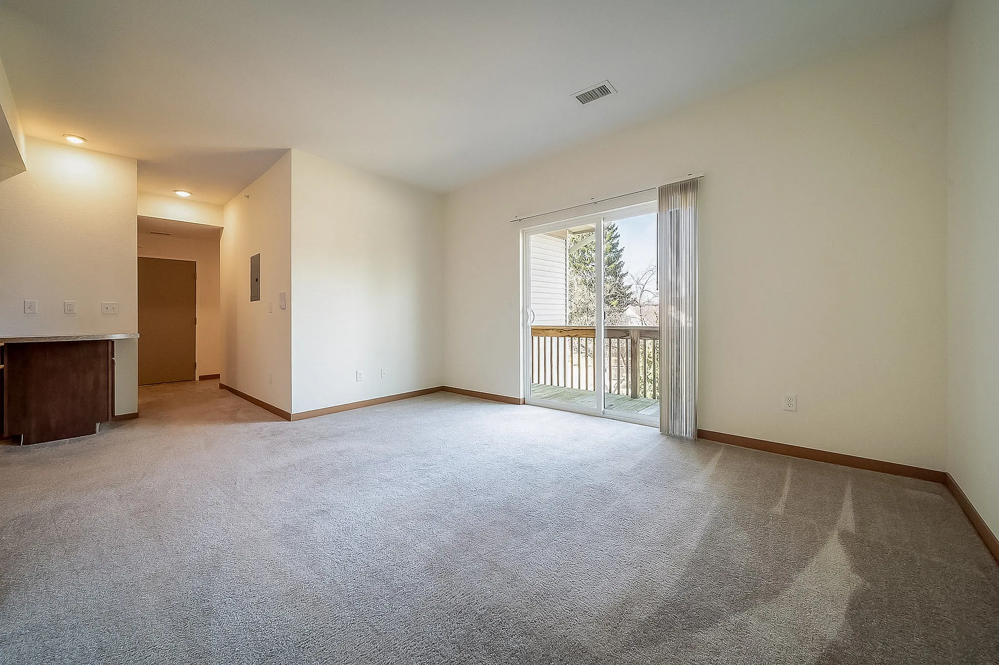 Bright living area with cozy carpet flooring, sliding glass doors leading to a scenic balcony, and ample natural light.