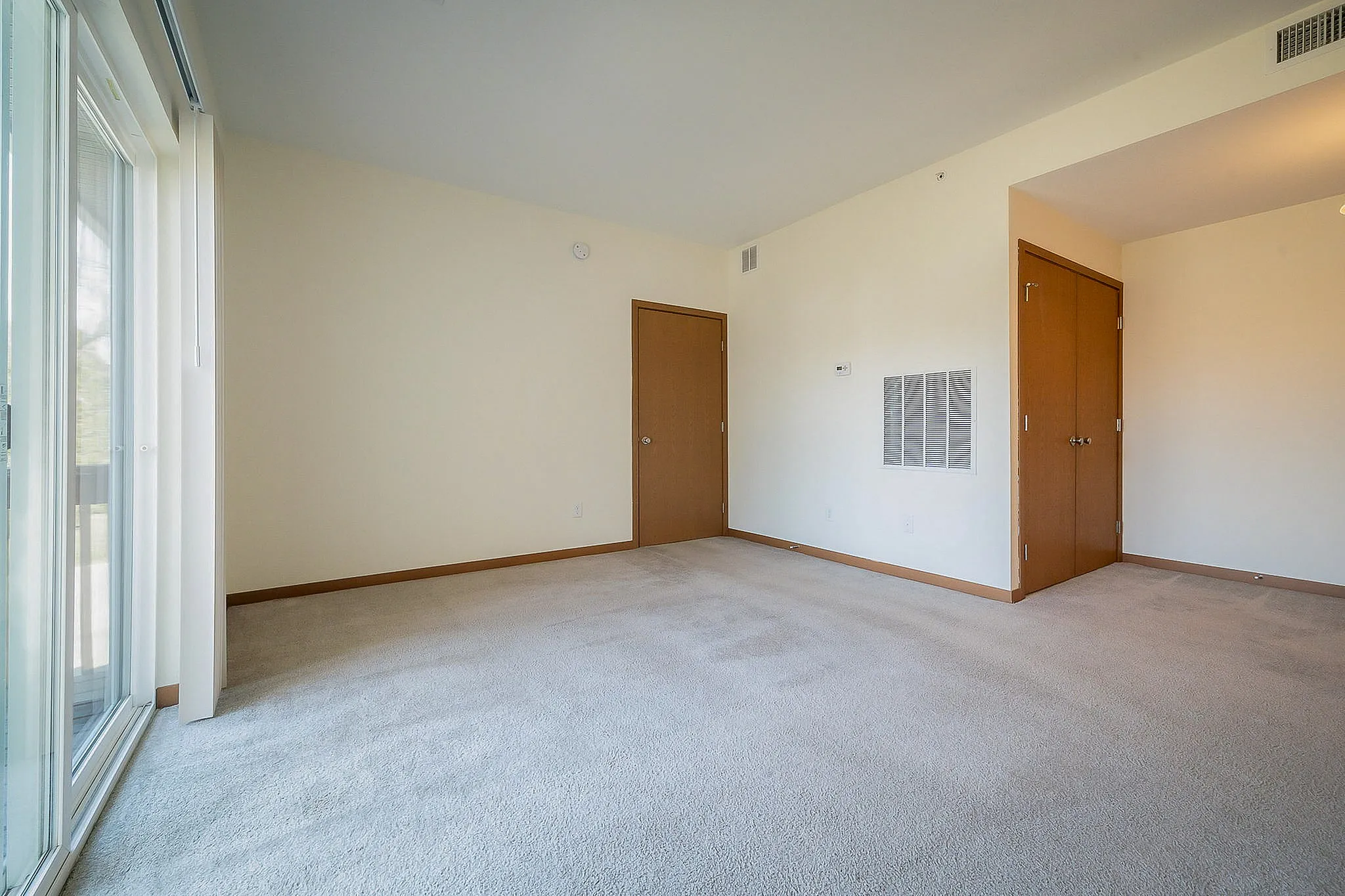 Bright and inviting living space with plush carpeting, large sliding glass doors, and neutral tones, perfect for personalization.