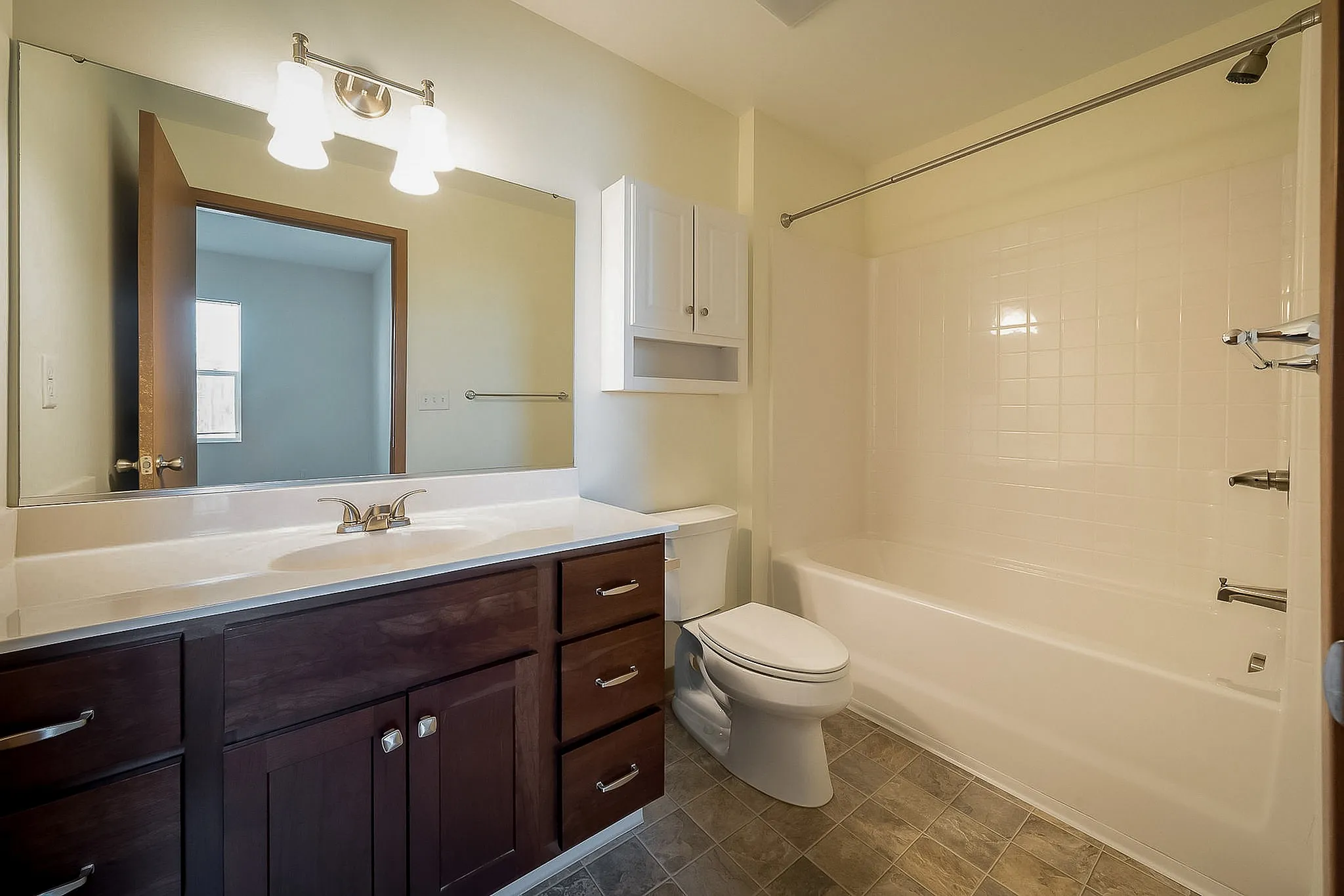 Bright and modern bathroom featuring elegant wood cabinetry, a large mirror, and a pristine bathtub, offering ultimate comfort and style.