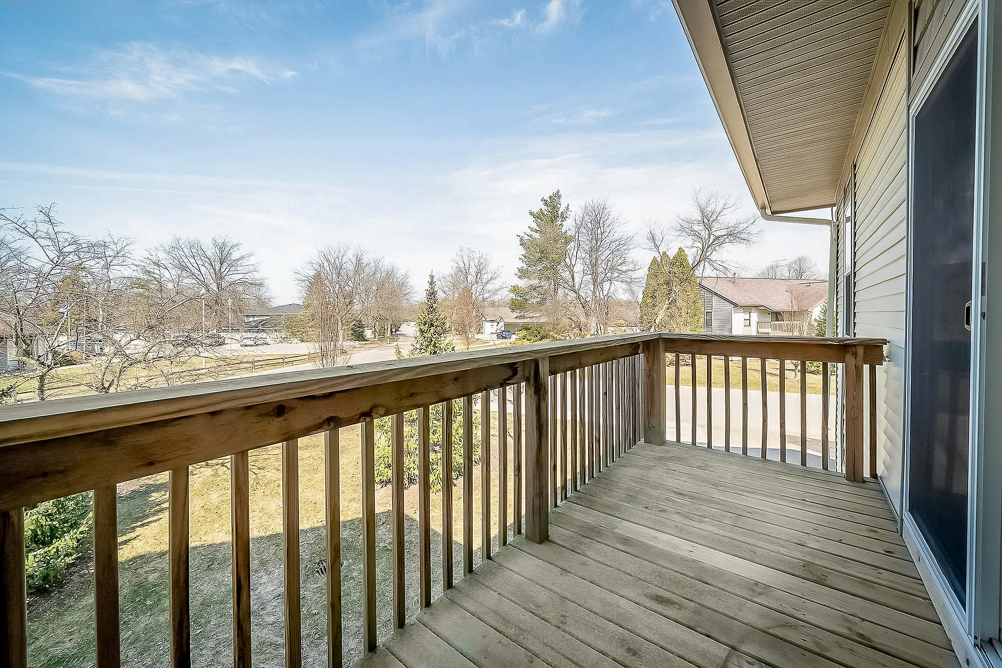 Charming wooden balcony overlooking a serene neighborhood with lush trees and blue skies.