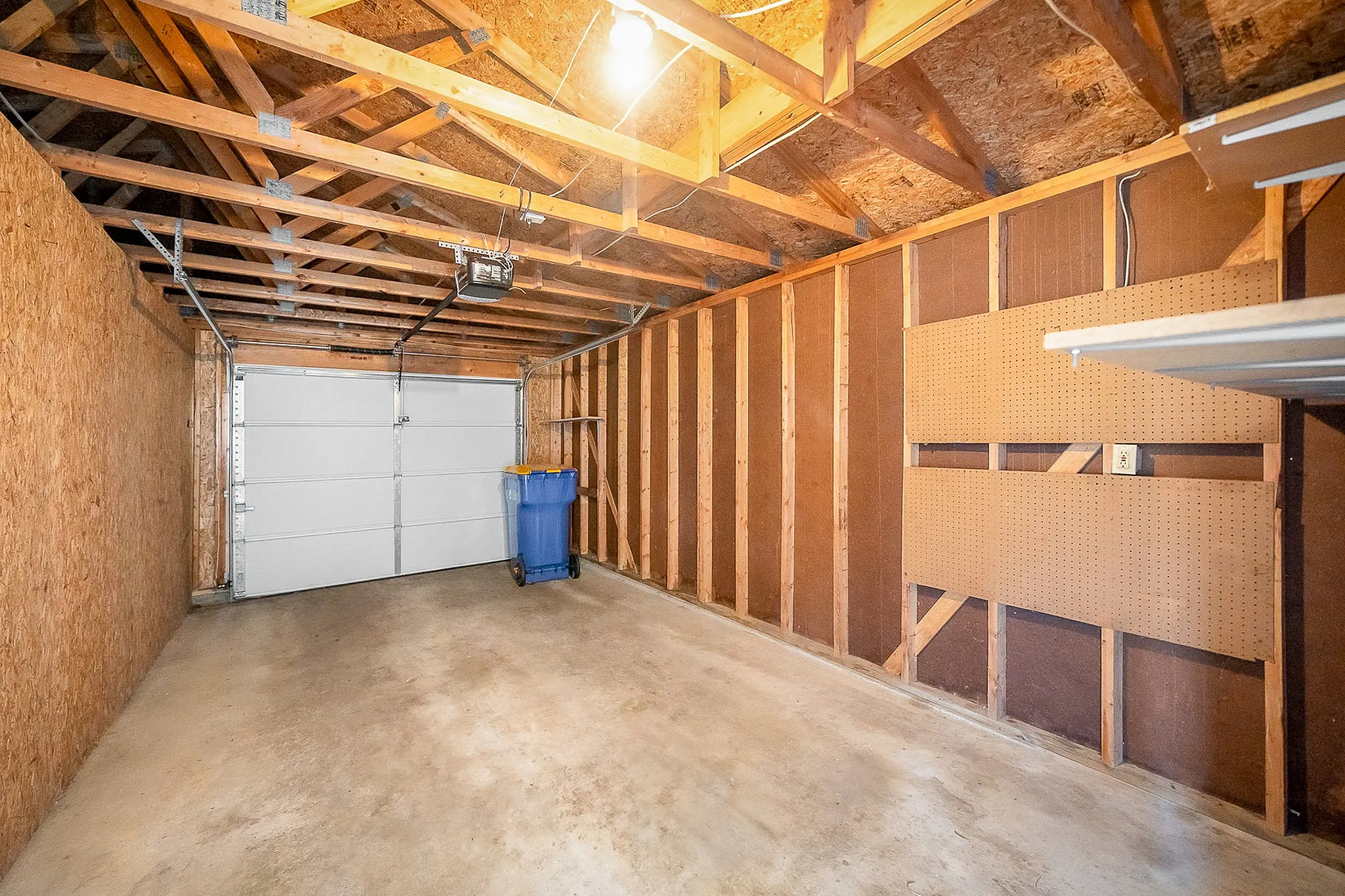Spacious garage with wooden rafters, ample storage space, and a large overhead door, perfect for secure parking and storage.
