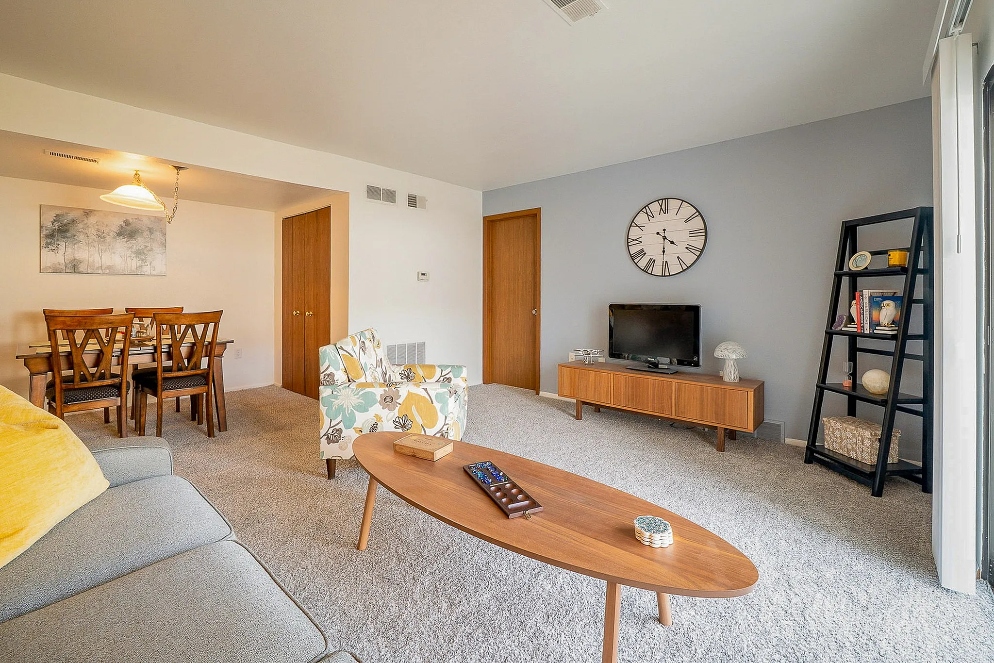 Bright and inviting living room with modern decor, featuring a cozy sofa, stylish armchair, and elegant dining area. Wide windows enhance natural light, creating a welcoming ambiance.
