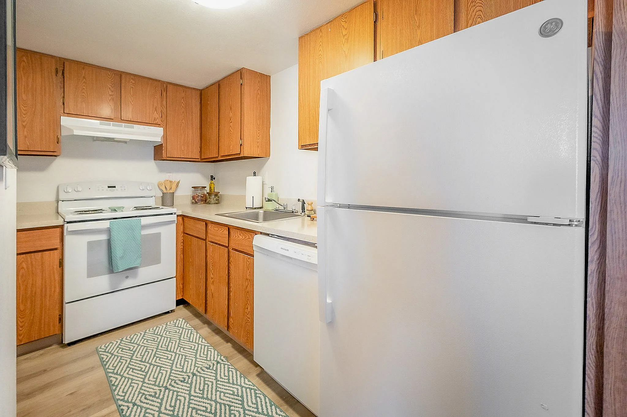 Charming kitchen with warm wooden cabinets, modern white appliances, and a cozy atmosphere. Perfect for culinary creativity.