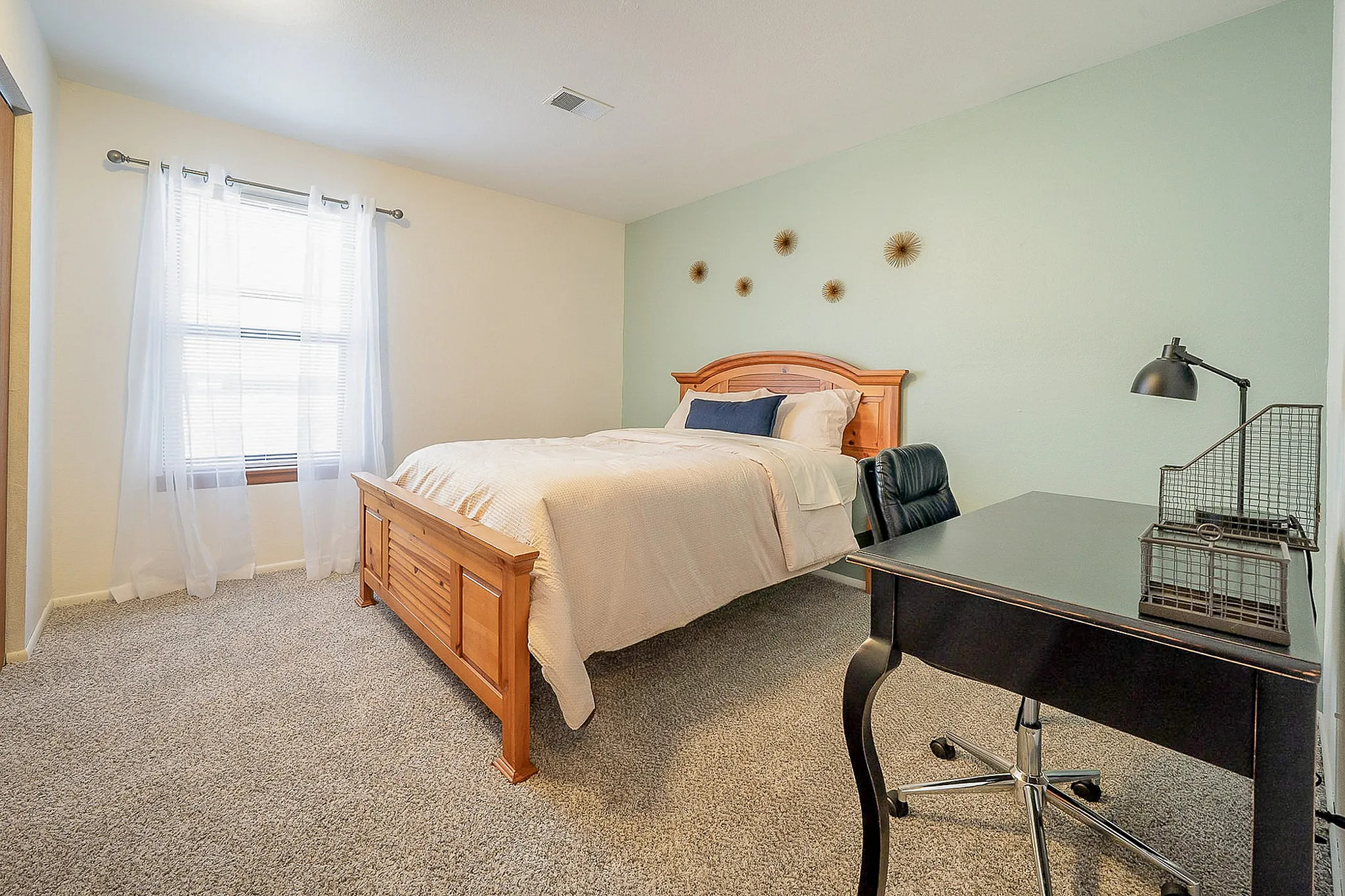 Inviting bedroom with cozy wooden bed, stylish decor, and a functional workspace under natural light.