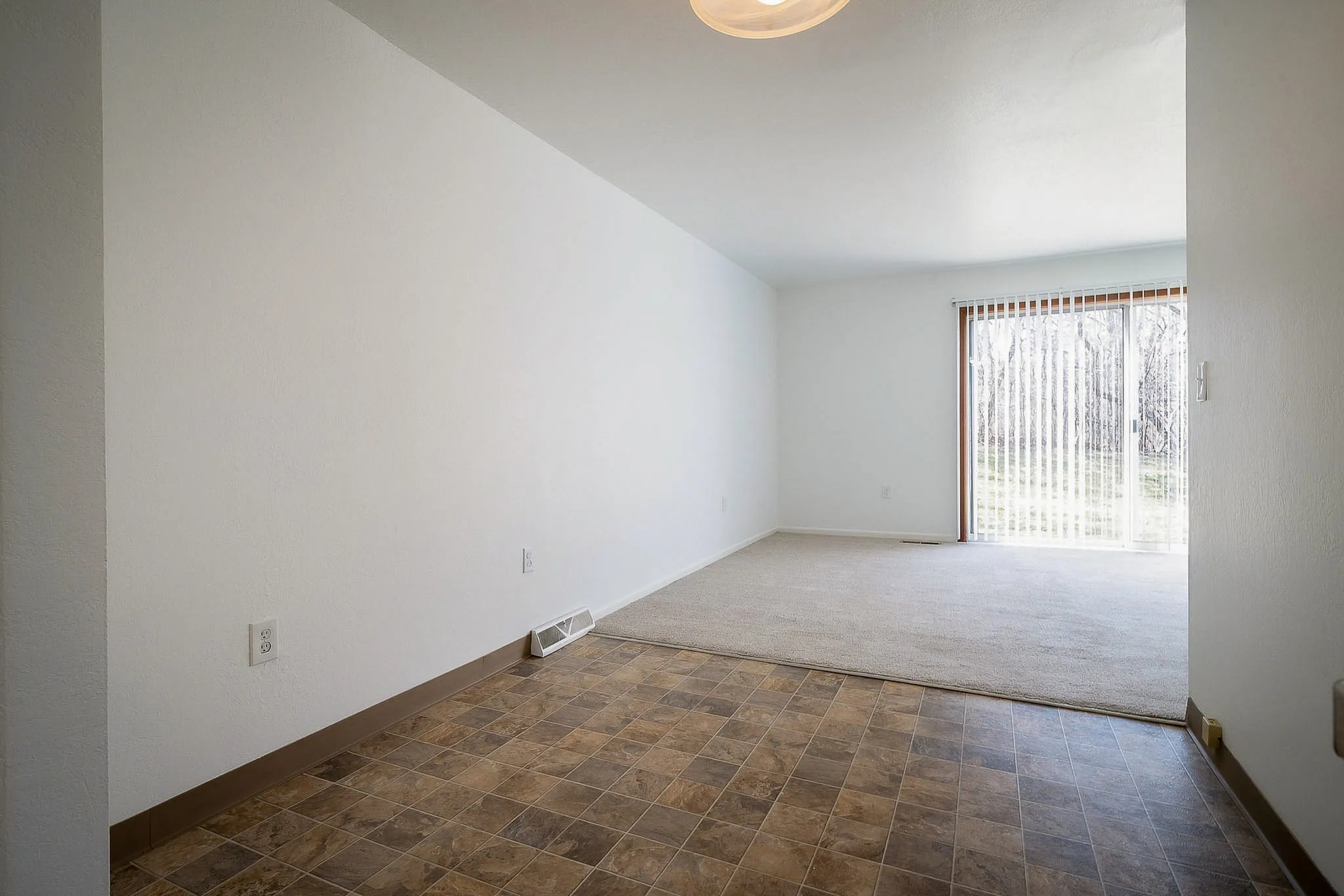 Bright open-plan living area featuring elegant tiled flooring, plush carpet, and large sliding glass doors with serene outdoor views.