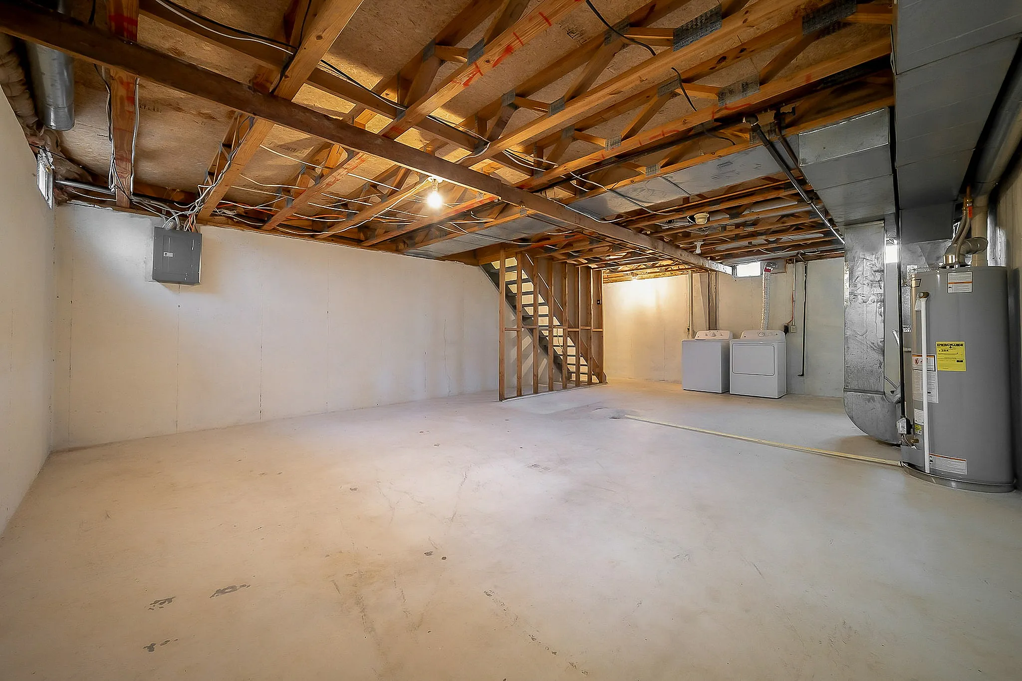 Expansive unfinished basement with washer and dryer, featuring exposed beams and ample potential for customization.