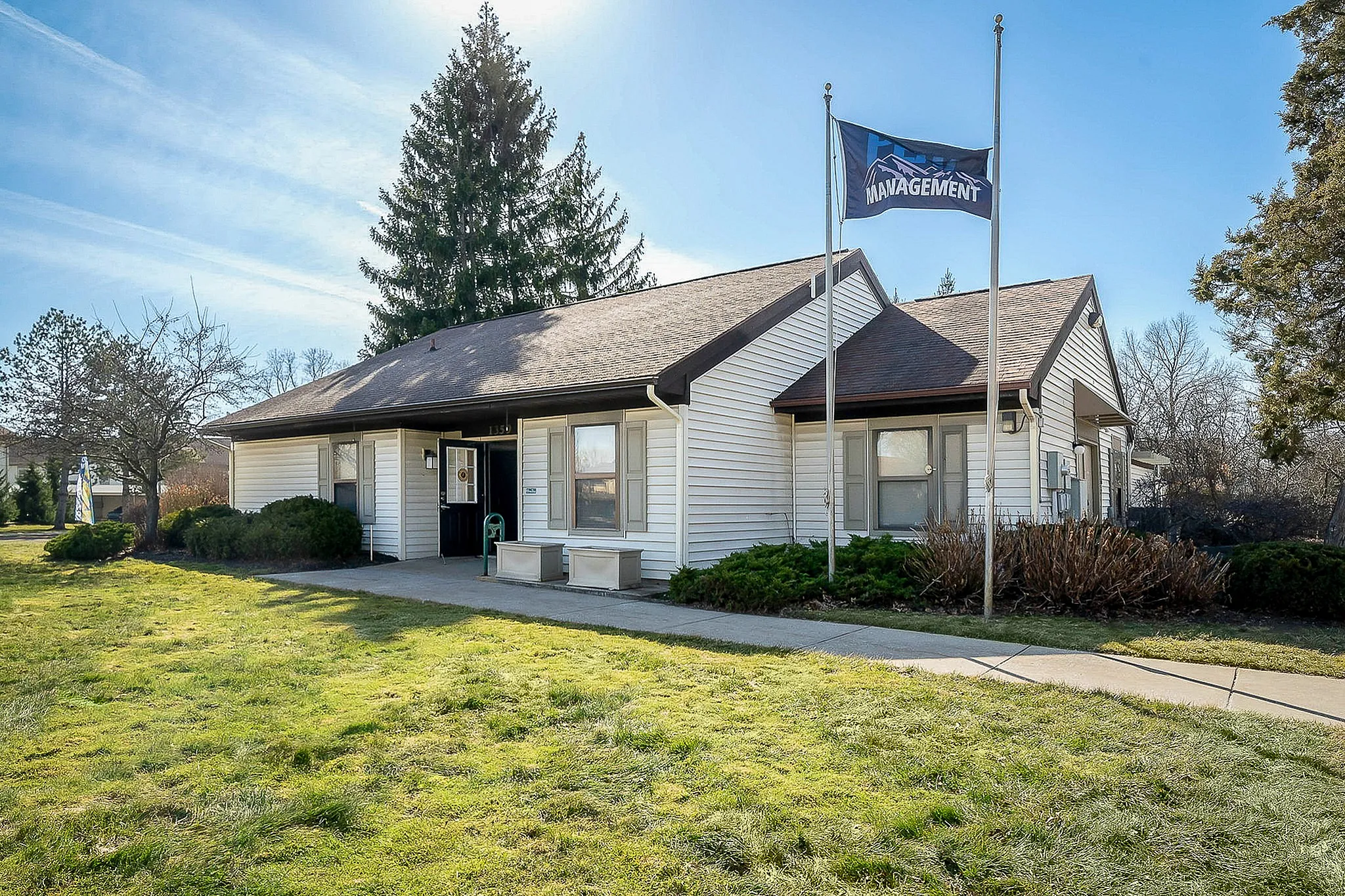 Charming management office with inviting exterior, manicured lawn, and welcoming walkway under a clear blue sky.