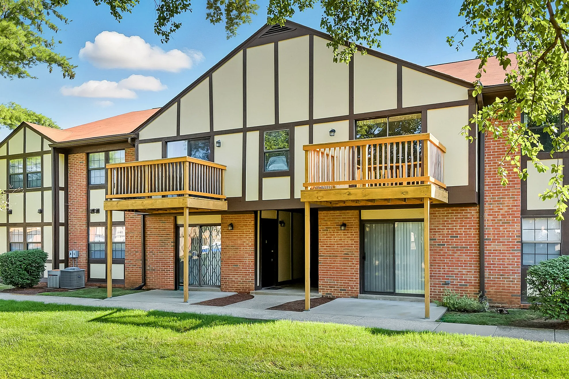 Charming apartment exterior with brick and timber accents, featuring private balconies and lush green lawns.