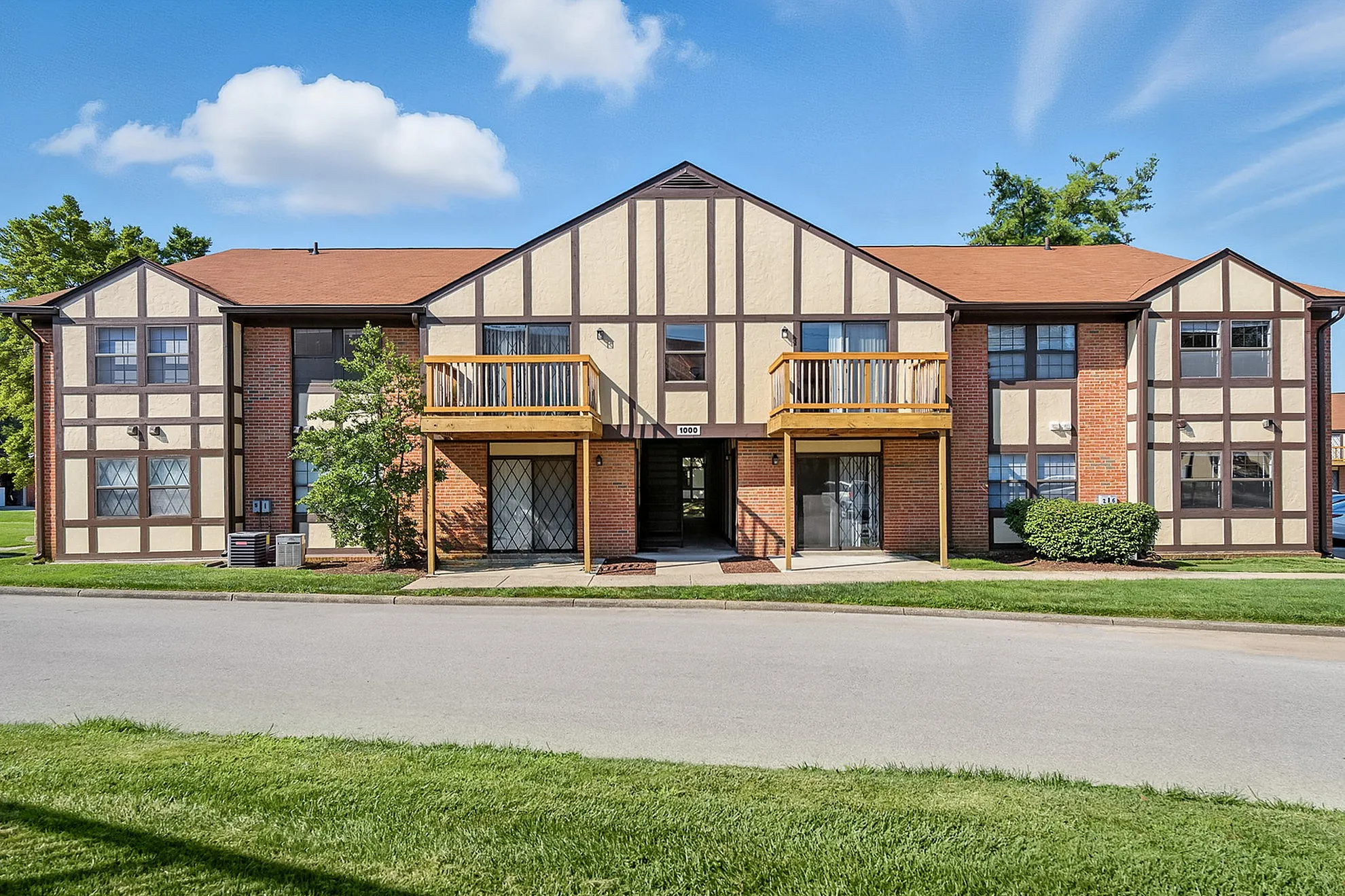 Charming Tudor-style apartment complex with spacious balconies, set against a clear blue sky and lush green surroundings.
