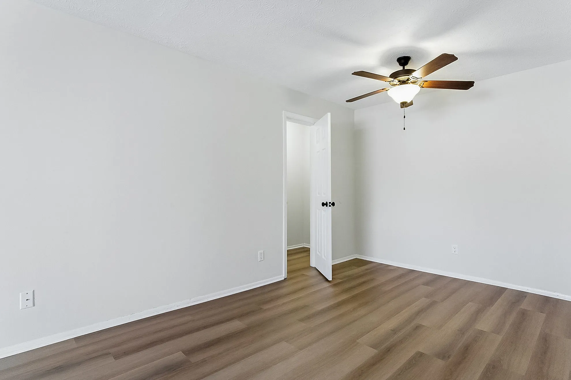 Bright and inviting bedroom featuring elegant wood flooring, a modern ceiling fan, and ample natural light.