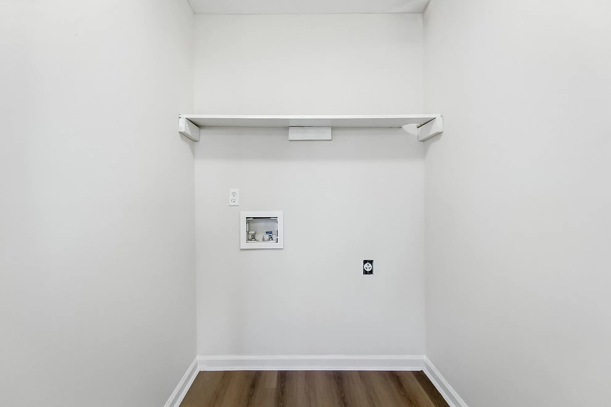 Modern utility room with sleek white walls, wooden flooring, and a convenient wall-mounted shelf for storage.