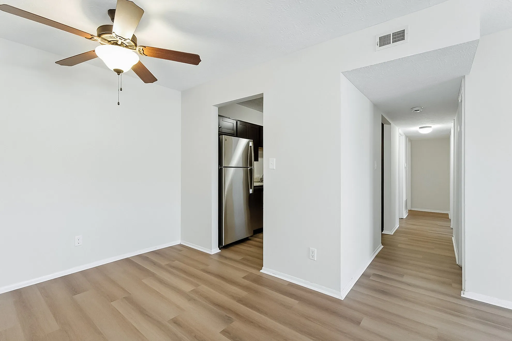 Modern apartment interior featuring sleek wood flooring, a ceiling fan, and a stylish stainless steel kitchen entrance.