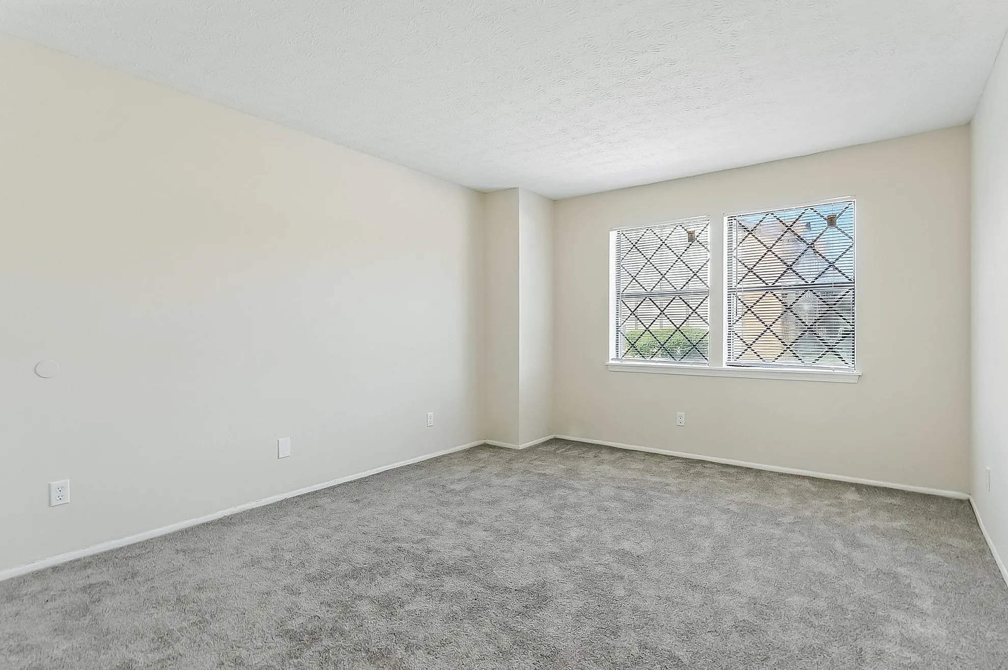 Bright and airy bedroom with plush carpeting and large windows featuring elegant grid-patterned blinds.