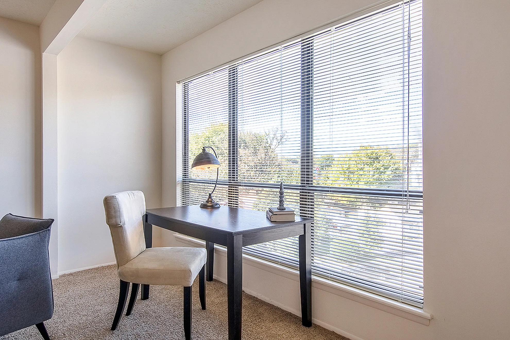Bright corner room with a sleek desk, cozy chair, and large windows offering scenic views, perfect for a home office setup.
