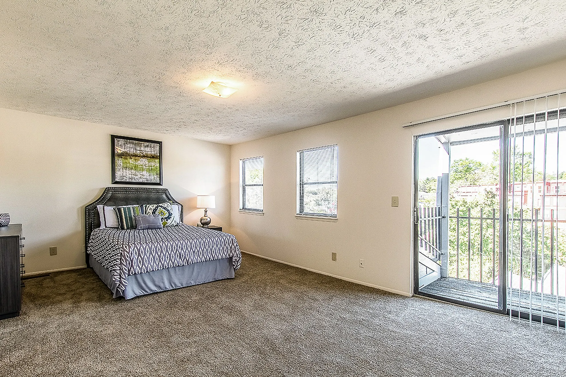 Sunlit bedroom with elegant decor, featuring a plush bed, modern nightstand, and access to a private balcony with scenic views.