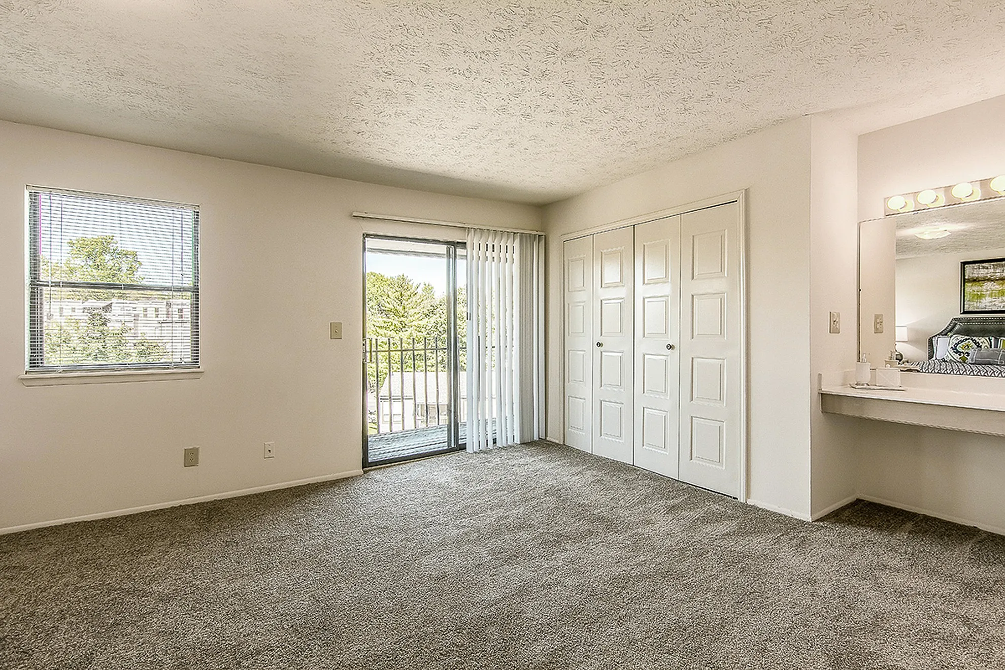 Bright and spacious bedroom with plush carpet, large closet, and access to a private balcony with serene views.