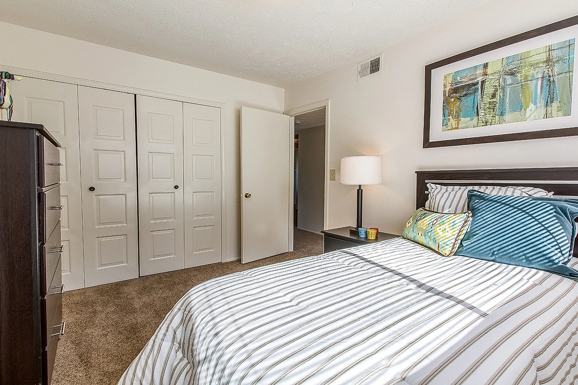 Bright and cozy bedroom with elegant striped bedding, modern art, and ample closet space, perfect for relaxation.
