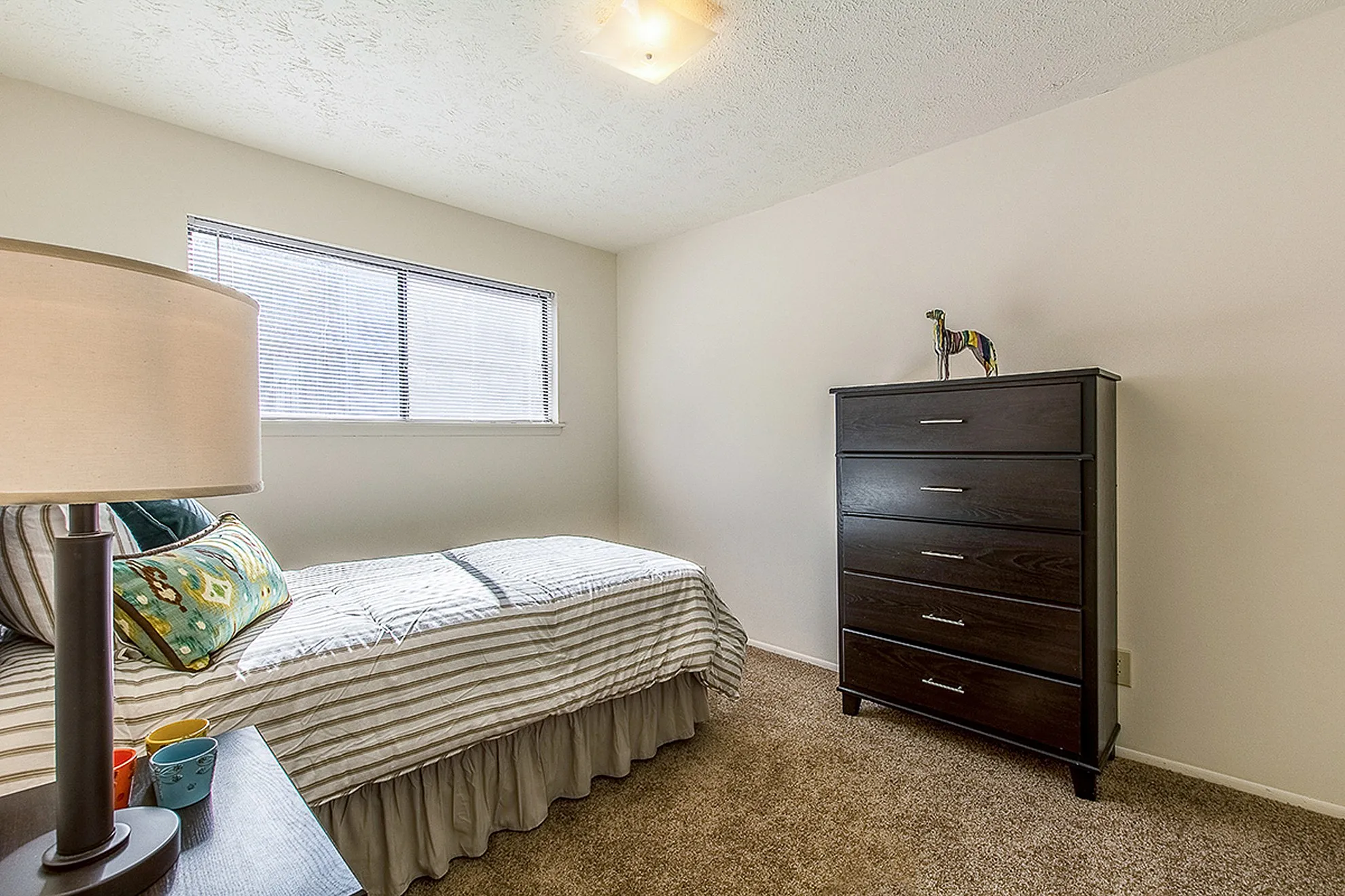 Bright and cozy bedroom with a sleek dresser, modern lamp, and a comfortable bed, perfect for relaxation.