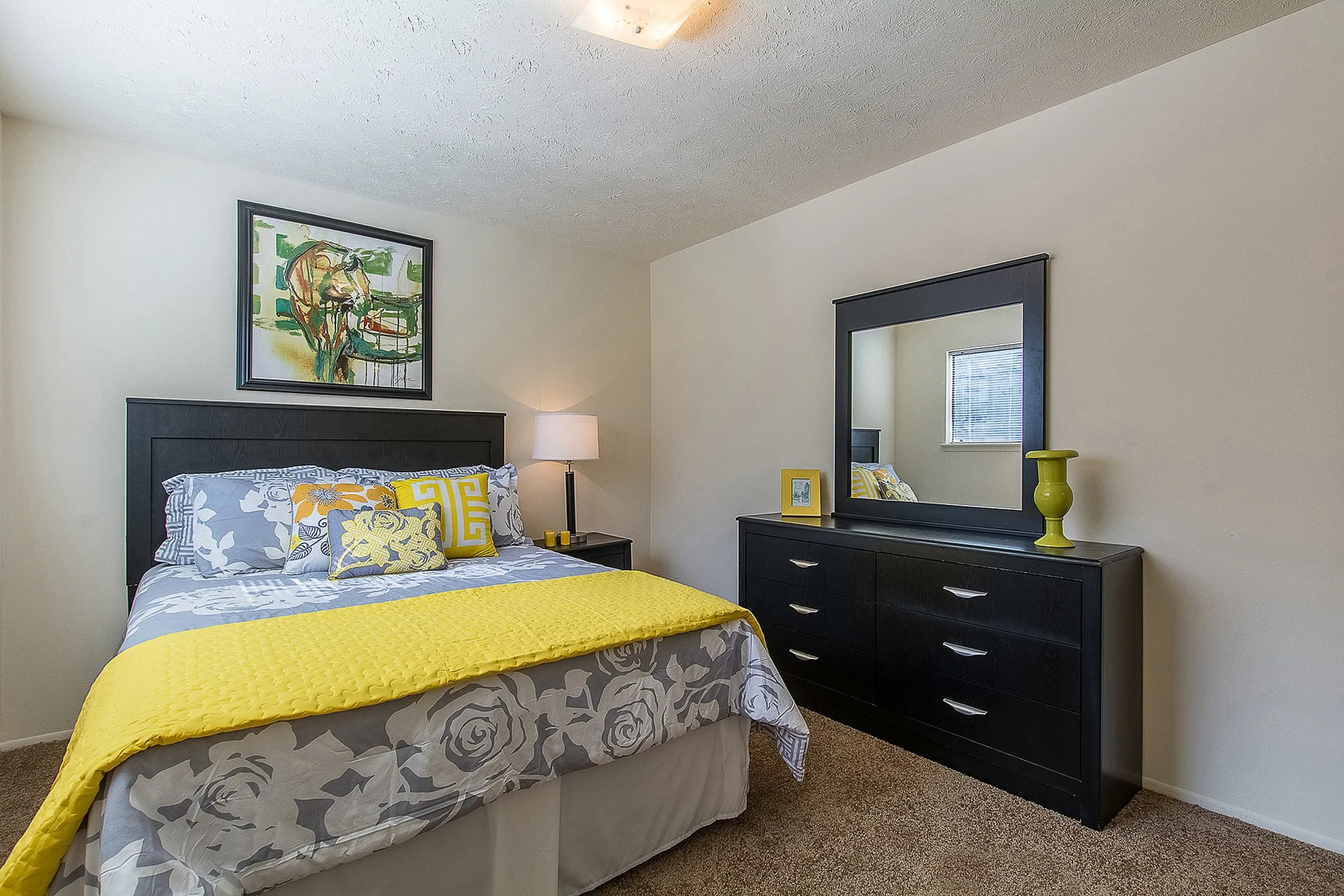 Inviting bedroom with modern decor, featuring a cozy bed with bright yellow accents and an elegant dresser with a large mirror.
