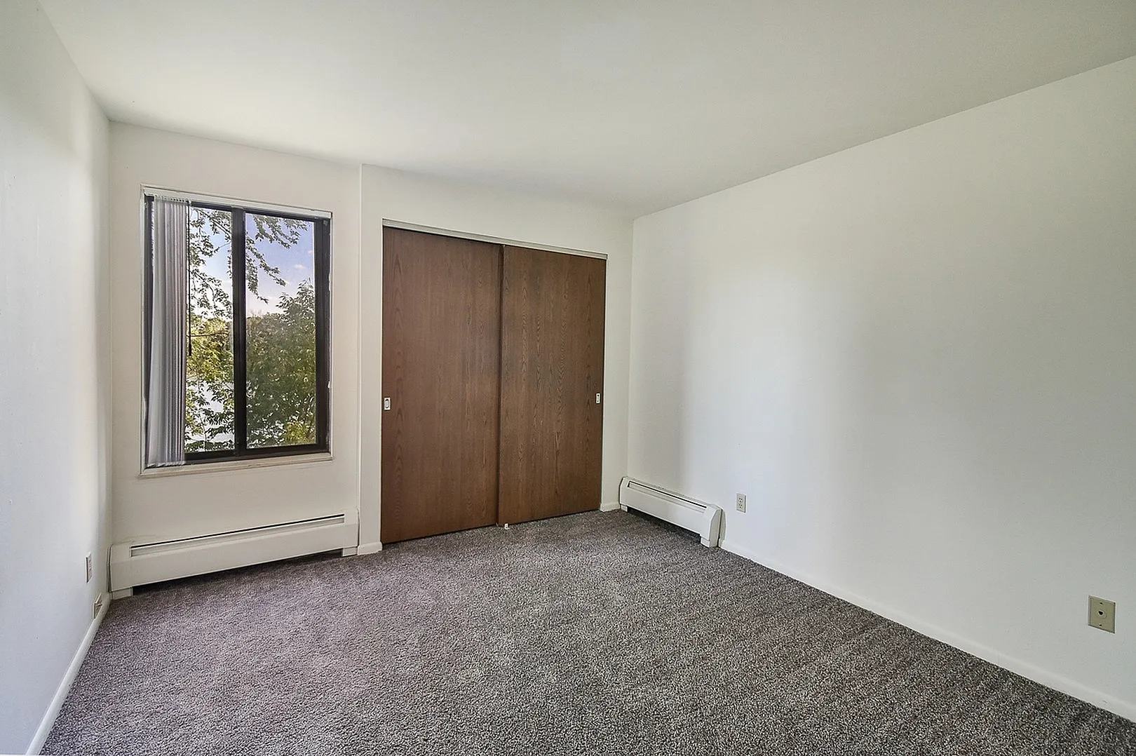 Bright bedroom featuring plush carpeting, large window with a calming view, and stylish wooden closet doors.