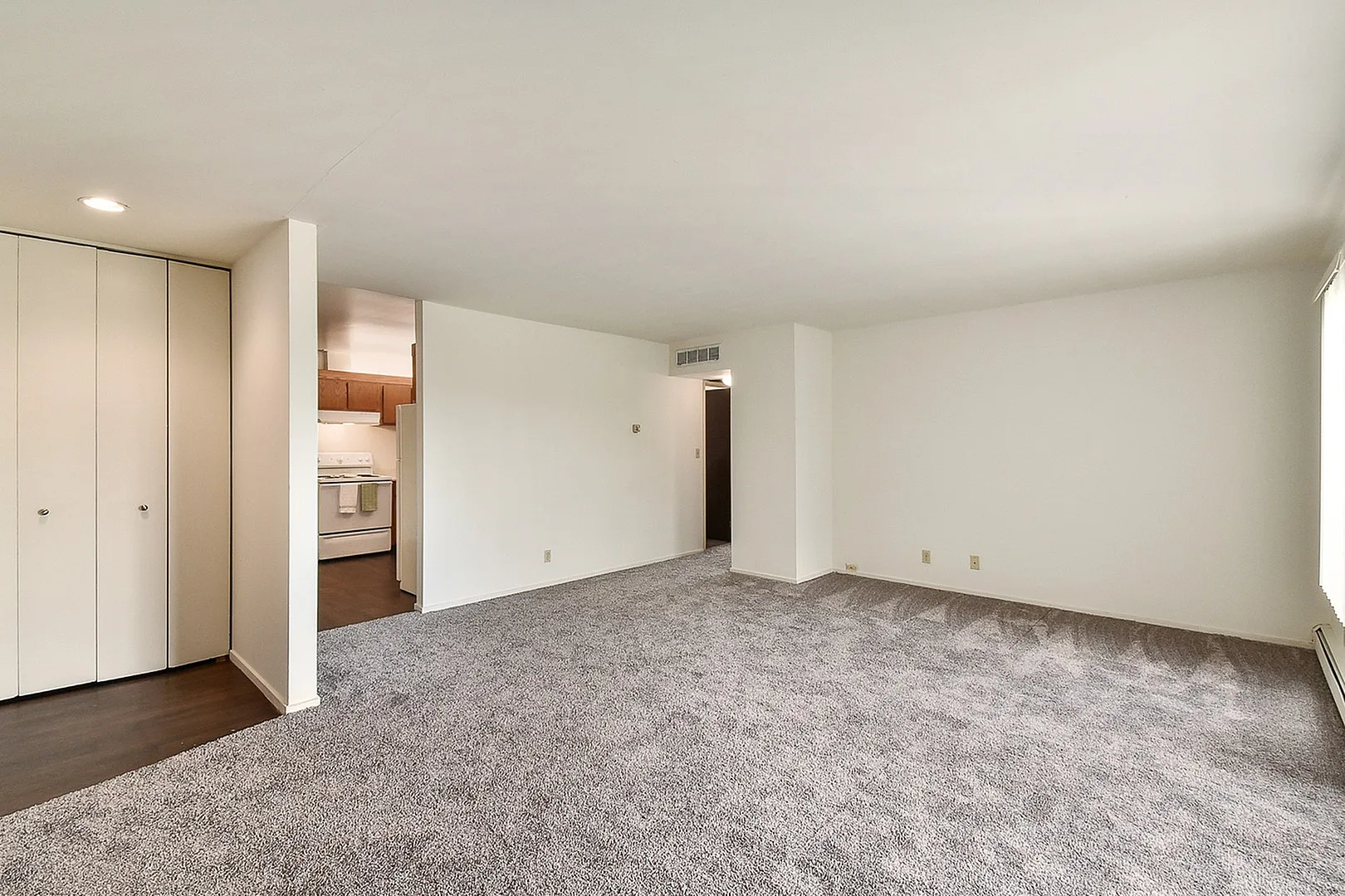 Spacious living area with plush carpet and adjacent kitchen, perfect for comfortable living and entertaining.