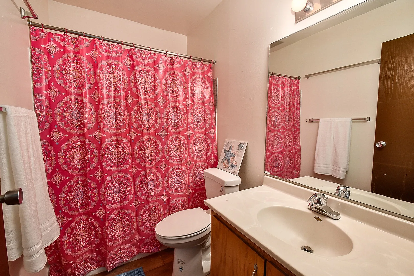 Vibrant bathroom with a bold pink patterned shower curtain, large mirror, and modern fixtures creating an inviting aesthetic.