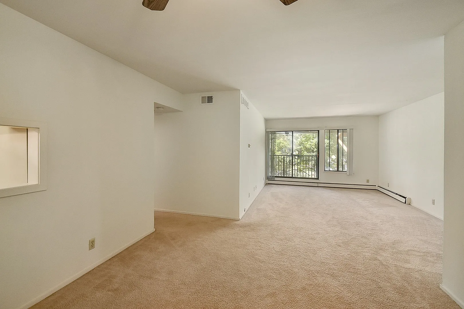 Spacious living room with plush carpeting and abundant natural light from large windows opening onto a balcony with a scenic view.