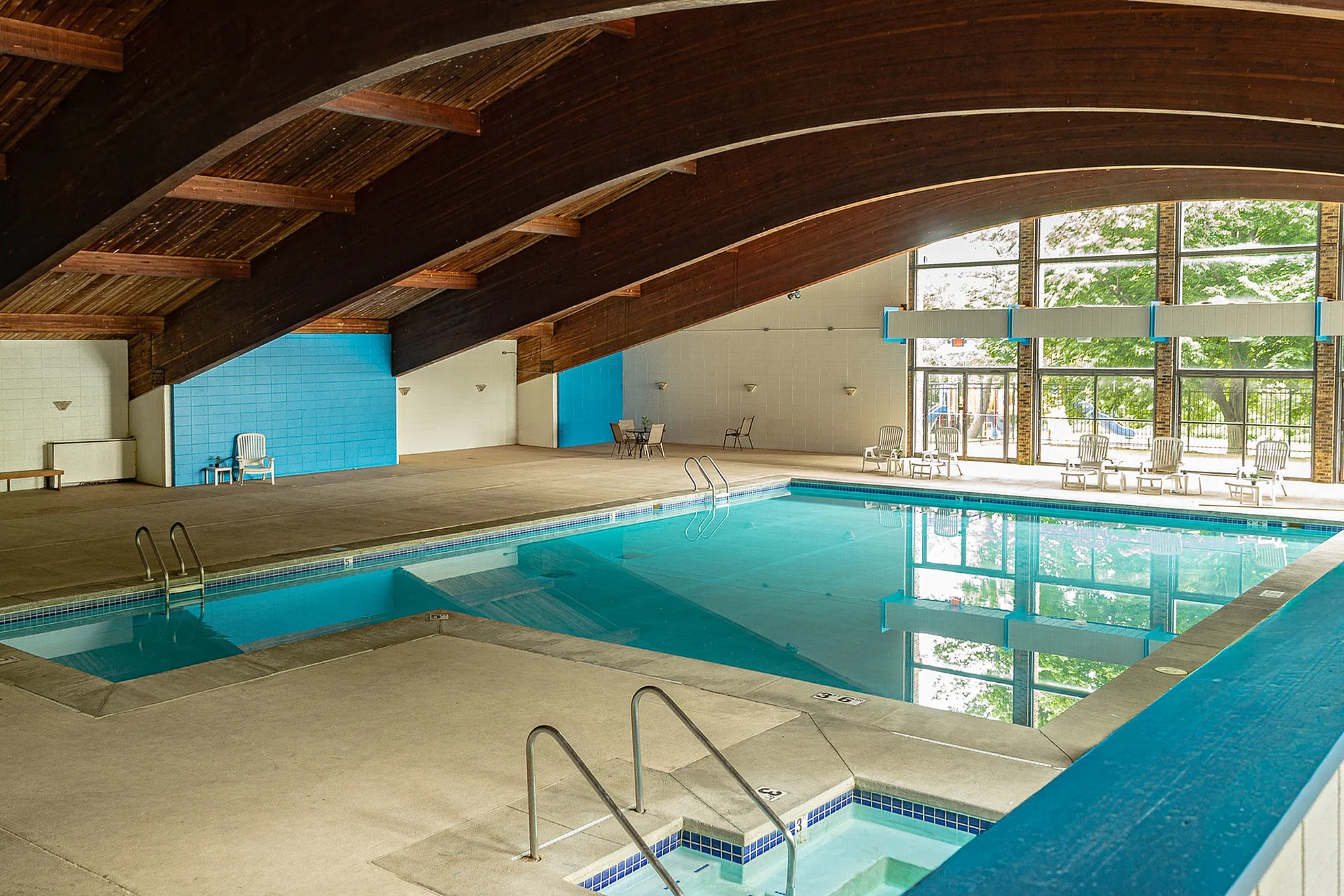 Luxurious indoor swimming pool with elegant wooden ceiling, large windows, and cozy seating area offering a serene escape.