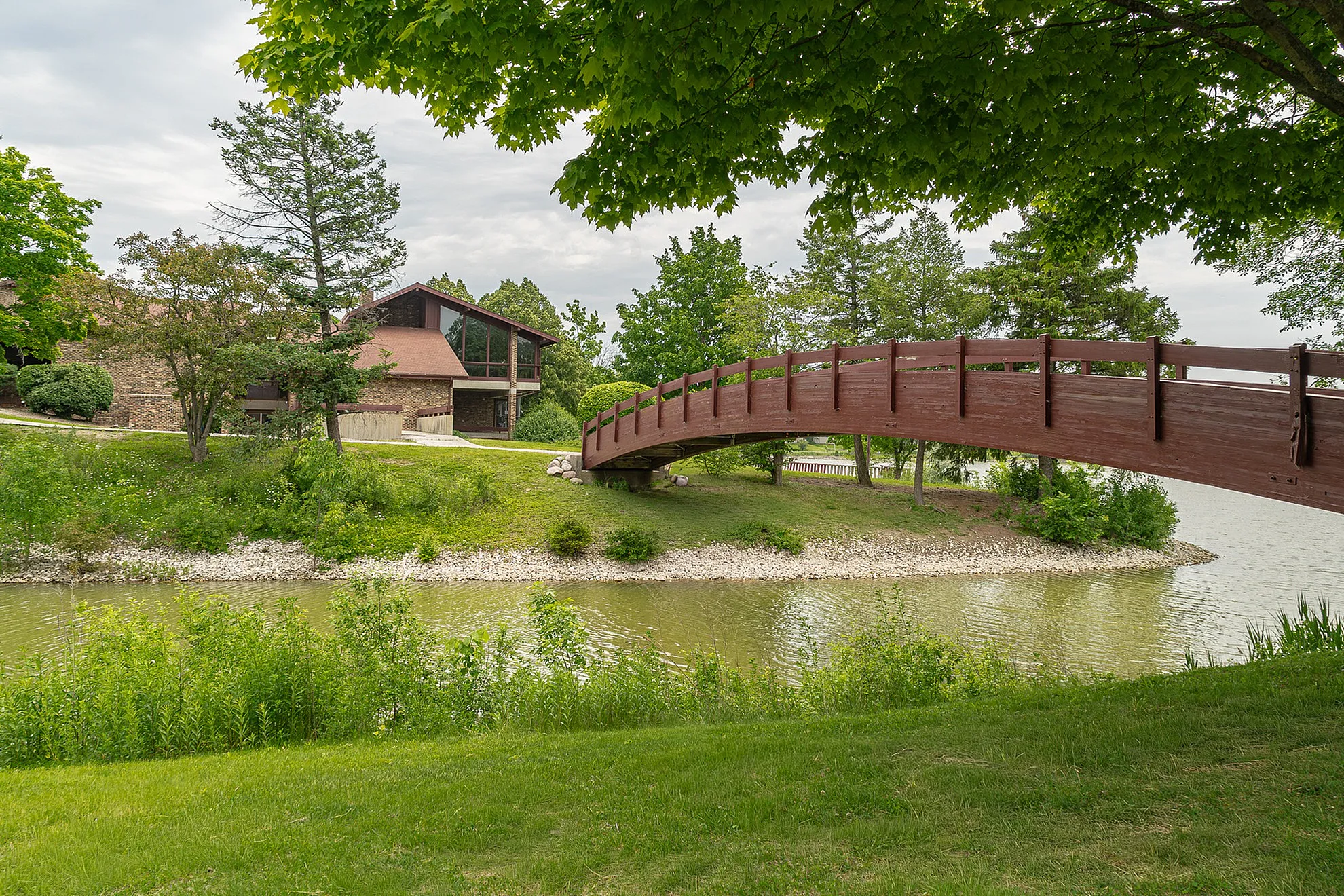 Charming riverside property featuring a rustic wooden bridge and lush landscaping with mature trees.