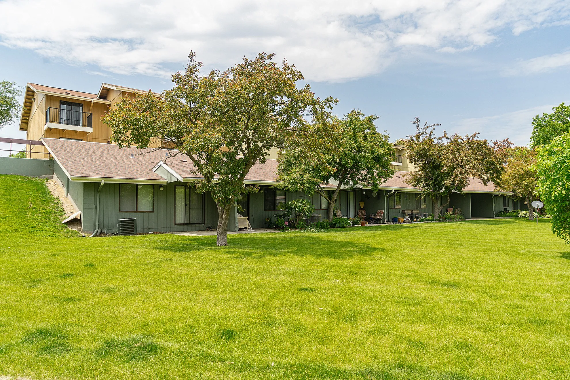 Charming residential building with lush green lawn and mature trees under a clear blue sky.