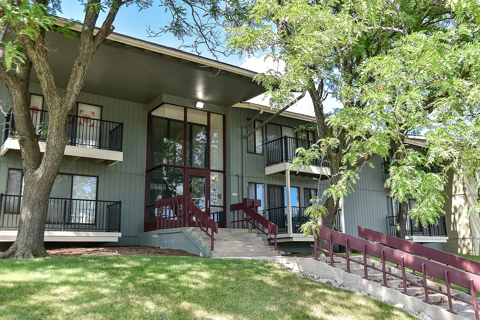 Charming two-story apartment building with floor-to-ceiling windows and private balconies surrounded by lush greenery.